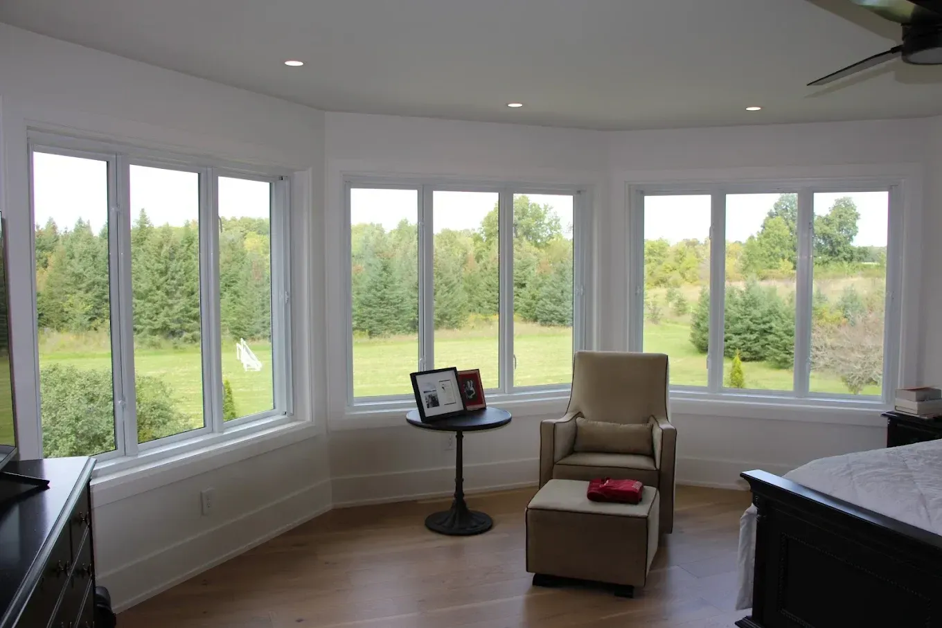 Bright room with large windows overlooking a green field. A chair, ottoman, and small table sit inside the bay window area.