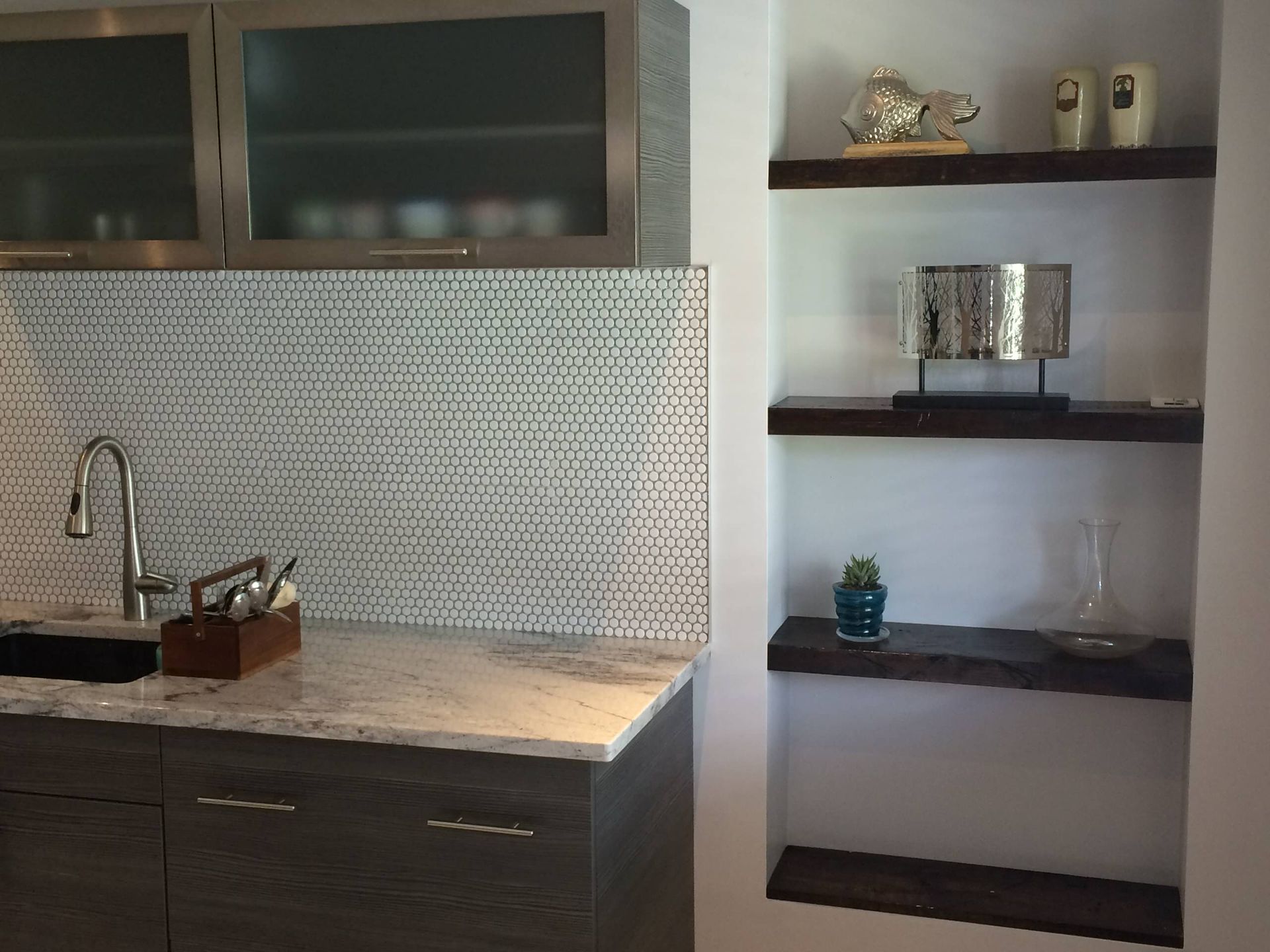 Kitchen with grey cabinets, stone countertop, mosaic backsplash, and built-in shelves.