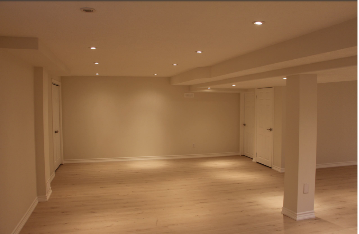Empty basement with white walls, columns, and recessed lighting. Light wood floor.