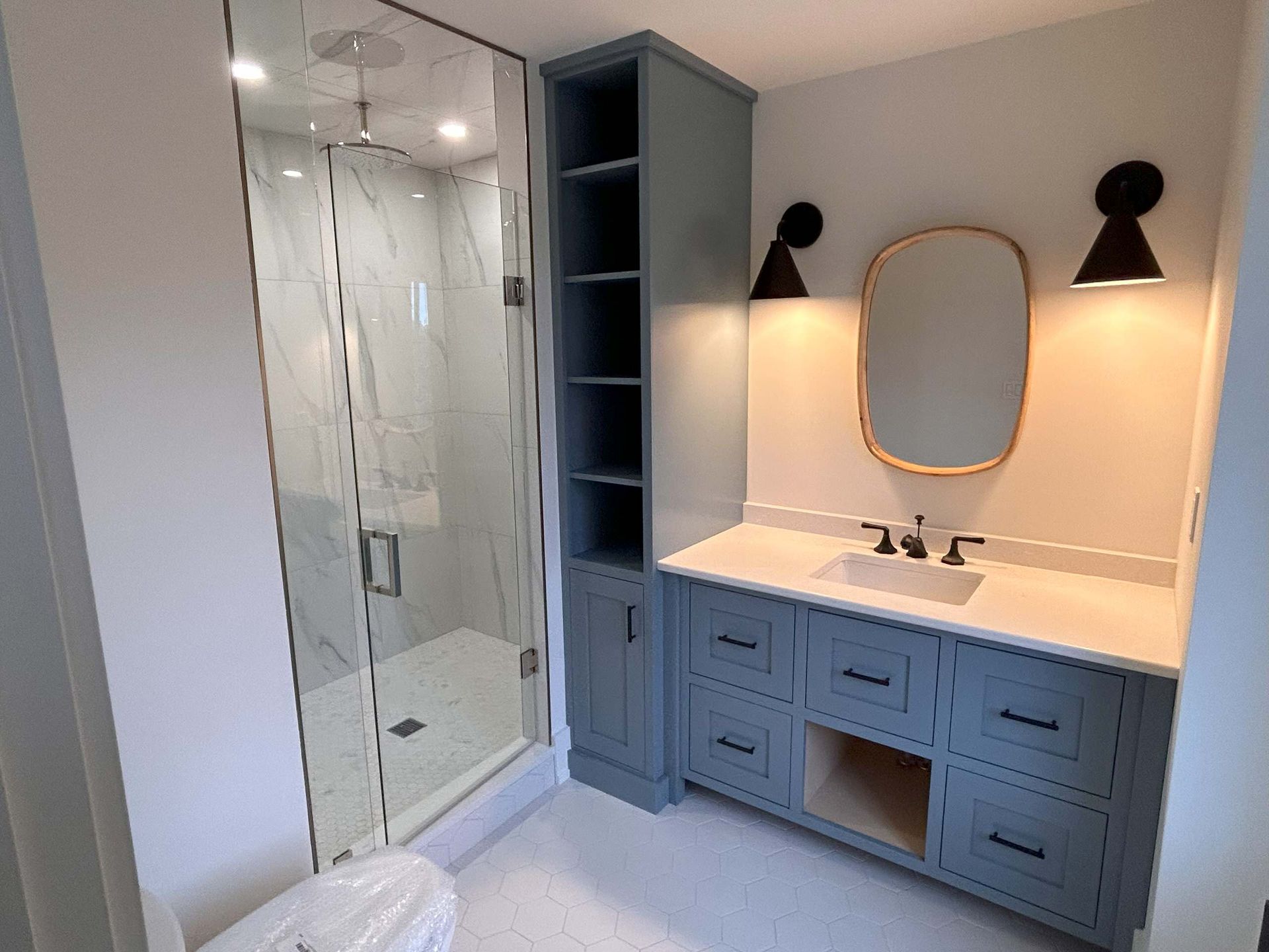 Bathroom with blue vanity, marble shower, open shelving, and sconces.
