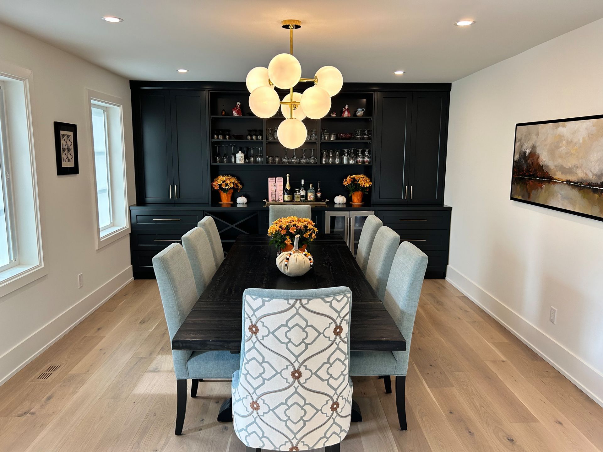 Elegant dining room with dark wood table, black built-in bar, globe chandelier, and light wood floors.