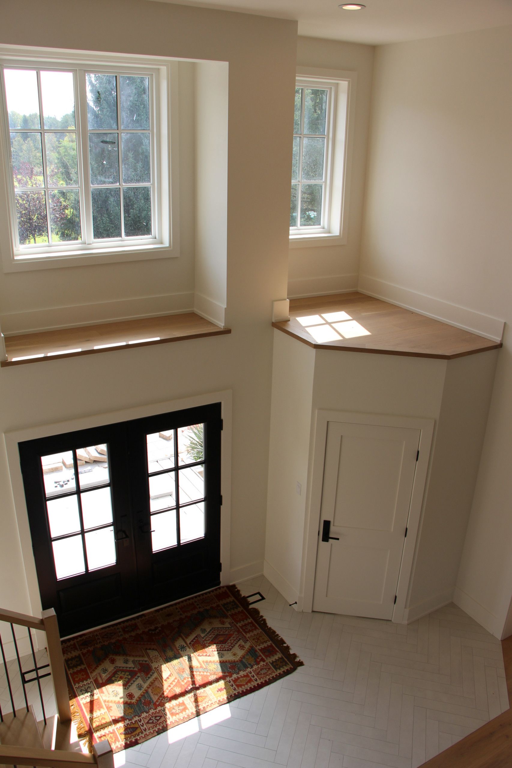 Two-story entryway with double black doors, windows, and white walls. A rug lies in front of the doors.