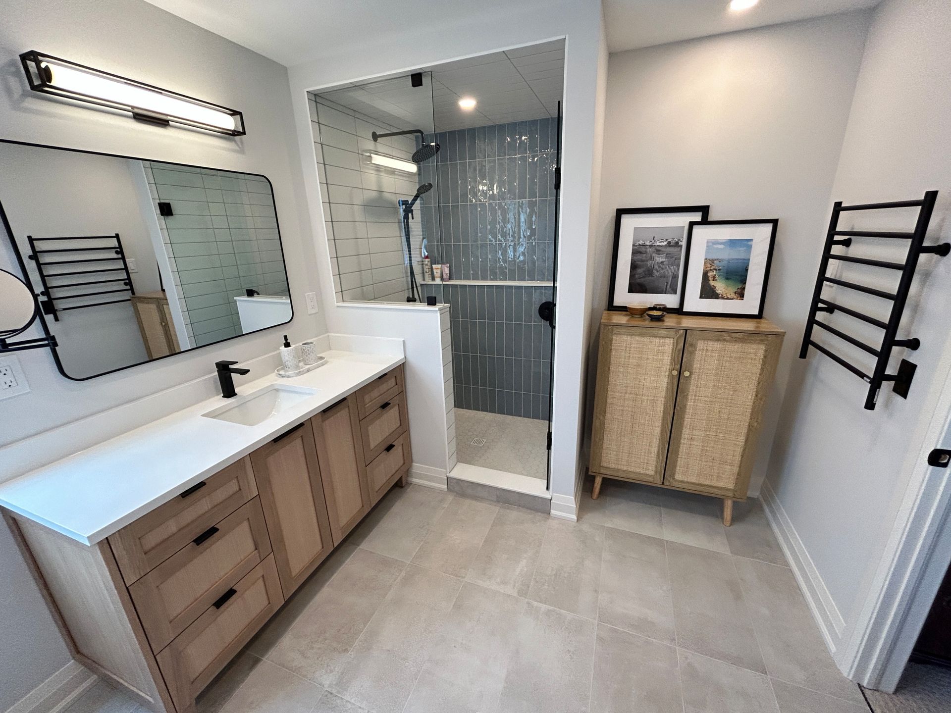 Modern bathroom with light wood vanity, glass shower, and gray tile.