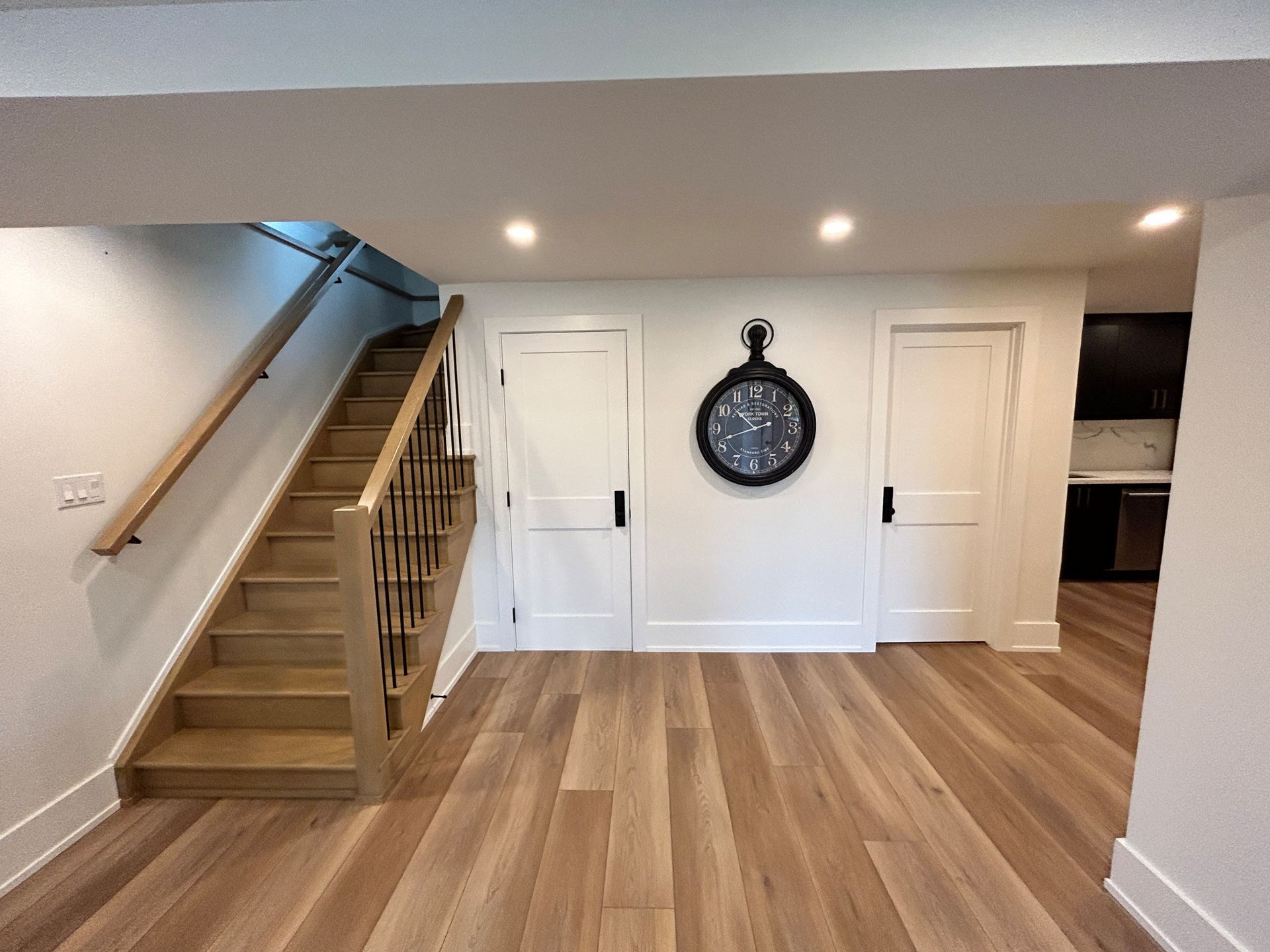 Staircase leads to a light wood floor and two white doors; clock on the wall.