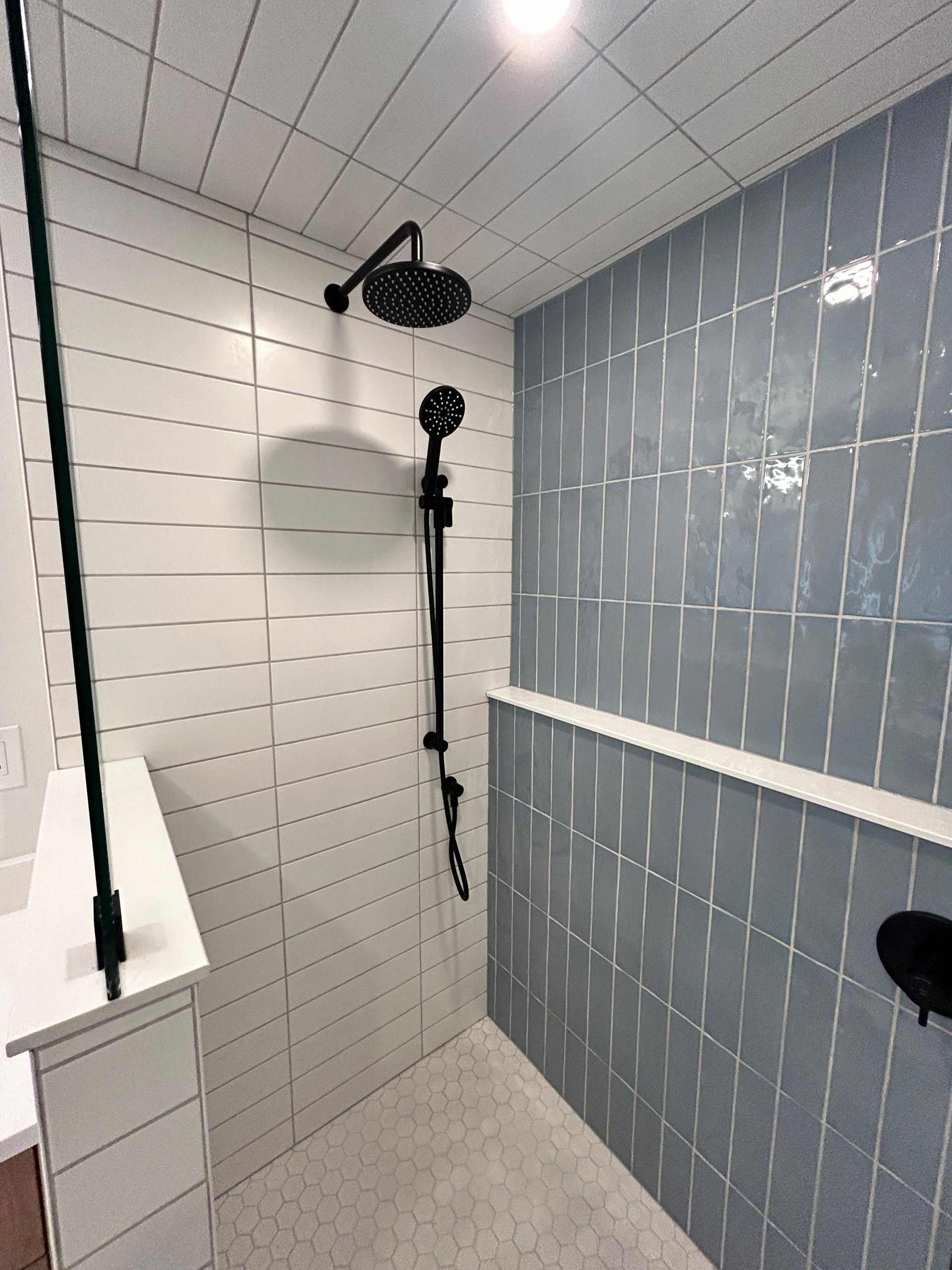 Modern bathroom shower with white and blue tiled walls, black shower fixtures.