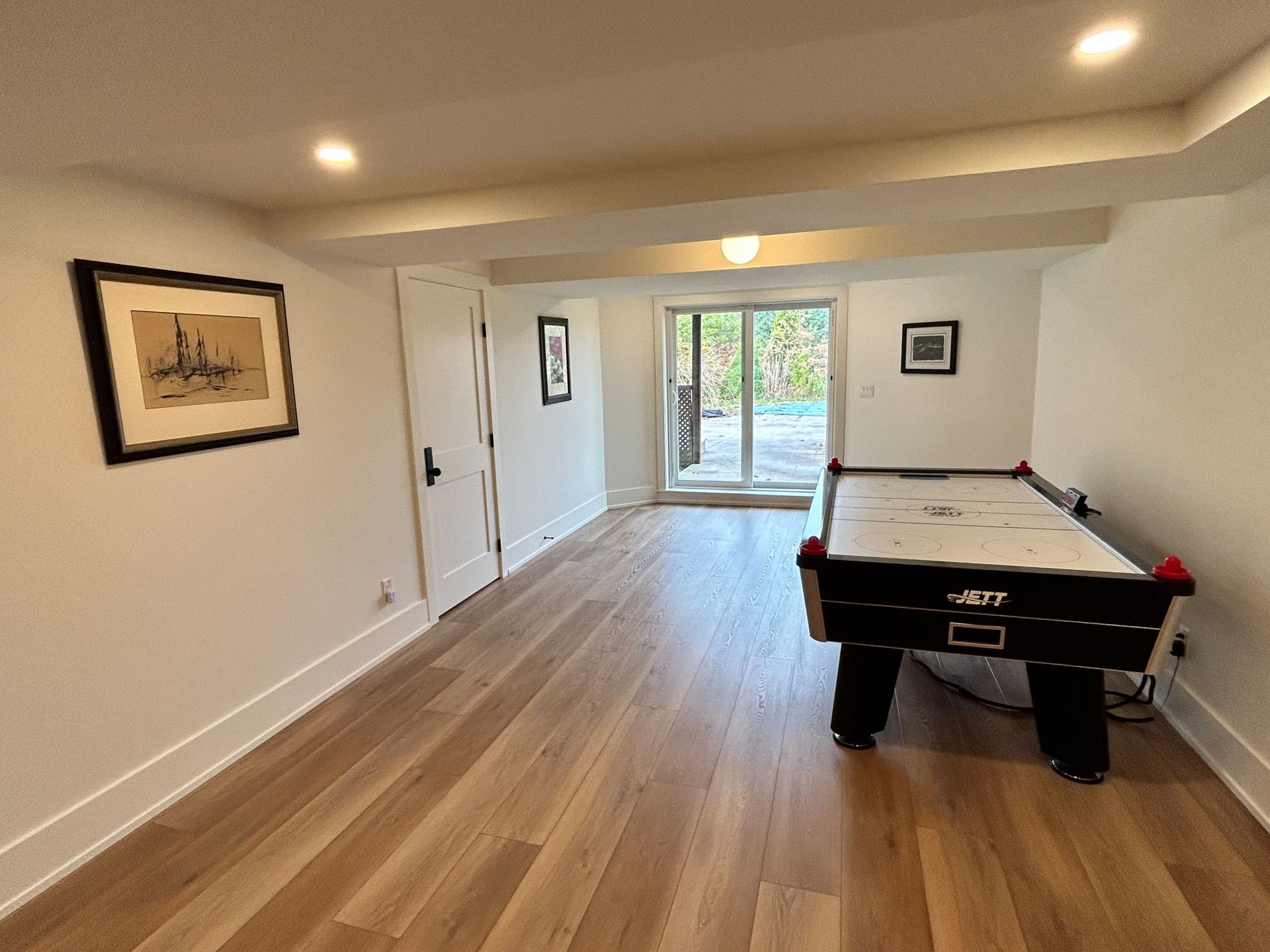 Basement with air hockey table, artwork, and door leading to outdoor area with wood flooring.