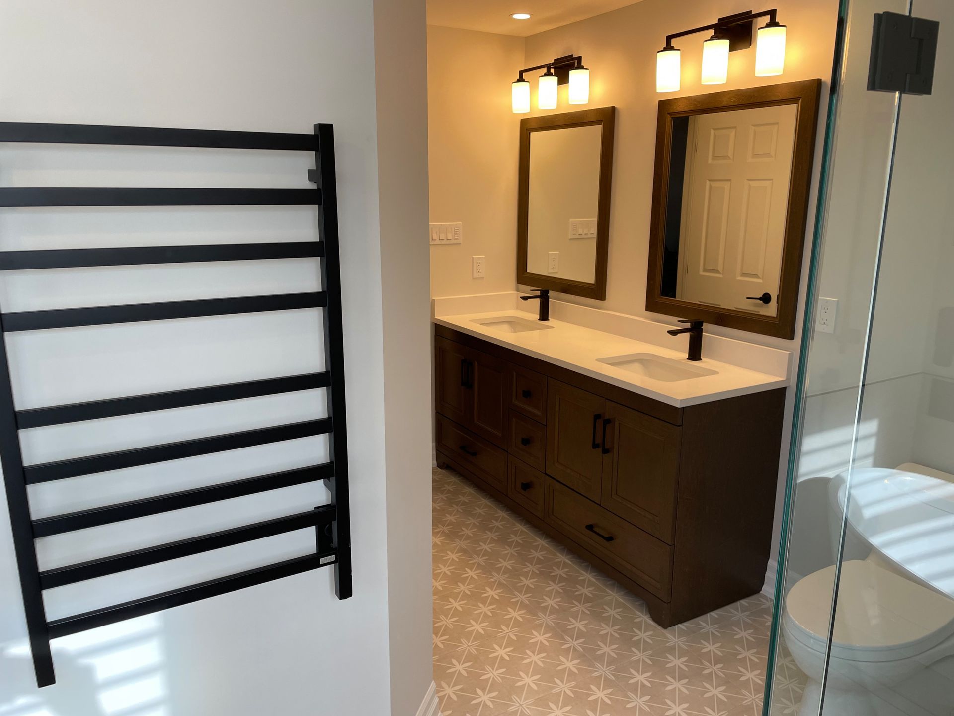 Modern bathroom with double vanity, black fixtures, heated towel rack, and patterned tile floor.