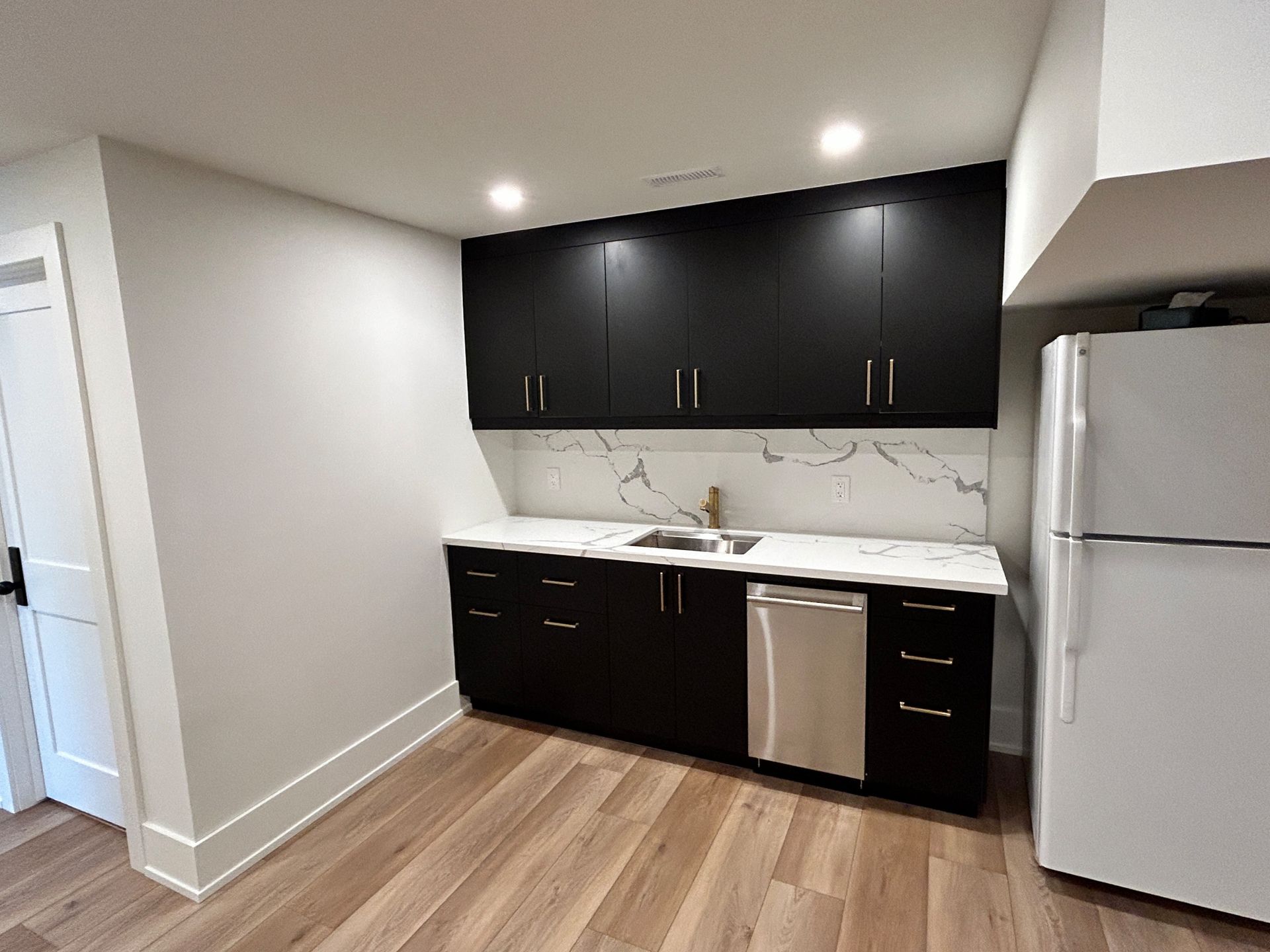 Black cabinets and white countertops in a small kitchen, with a stainless steel sink and dishwasher.