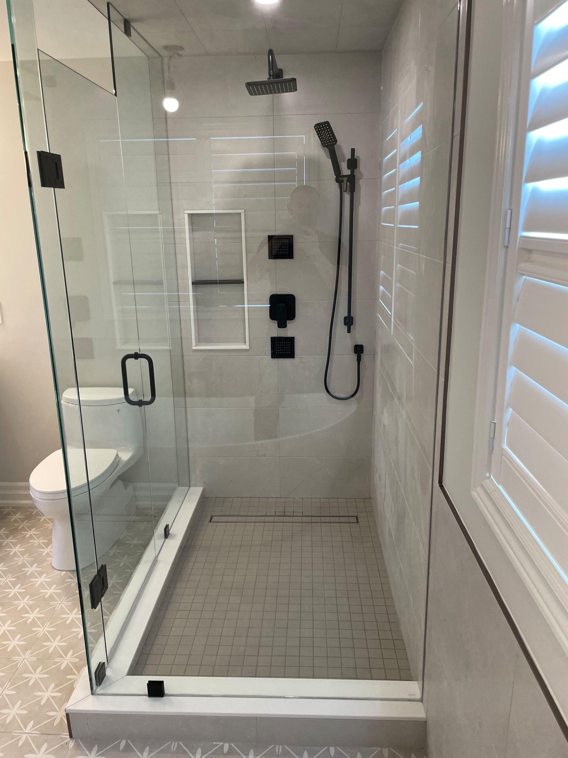 Modern bathroom with glass shower, black fixtures, white tile, and a toilet.