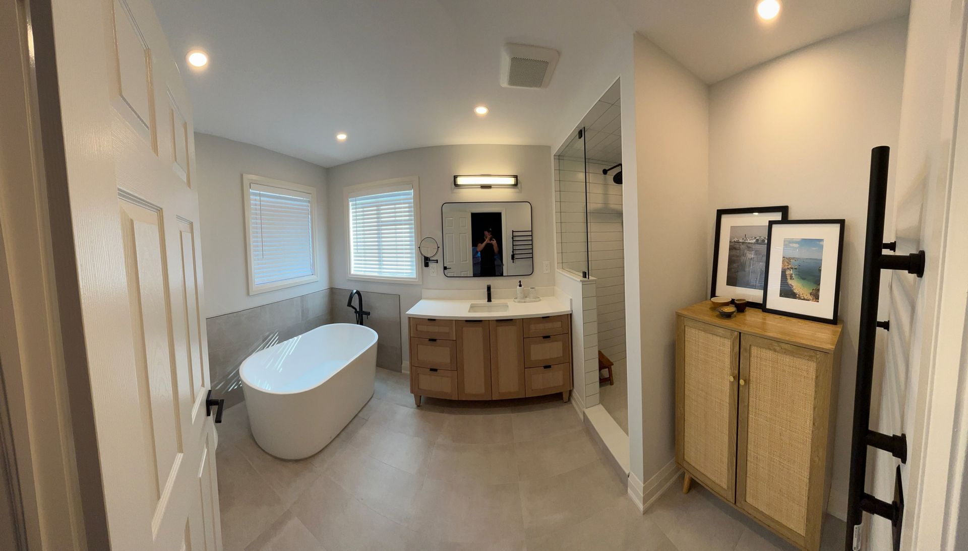 Spacious bathroom with a freestanding tub, wood vanity, shower, and art. Light and neutral colors.