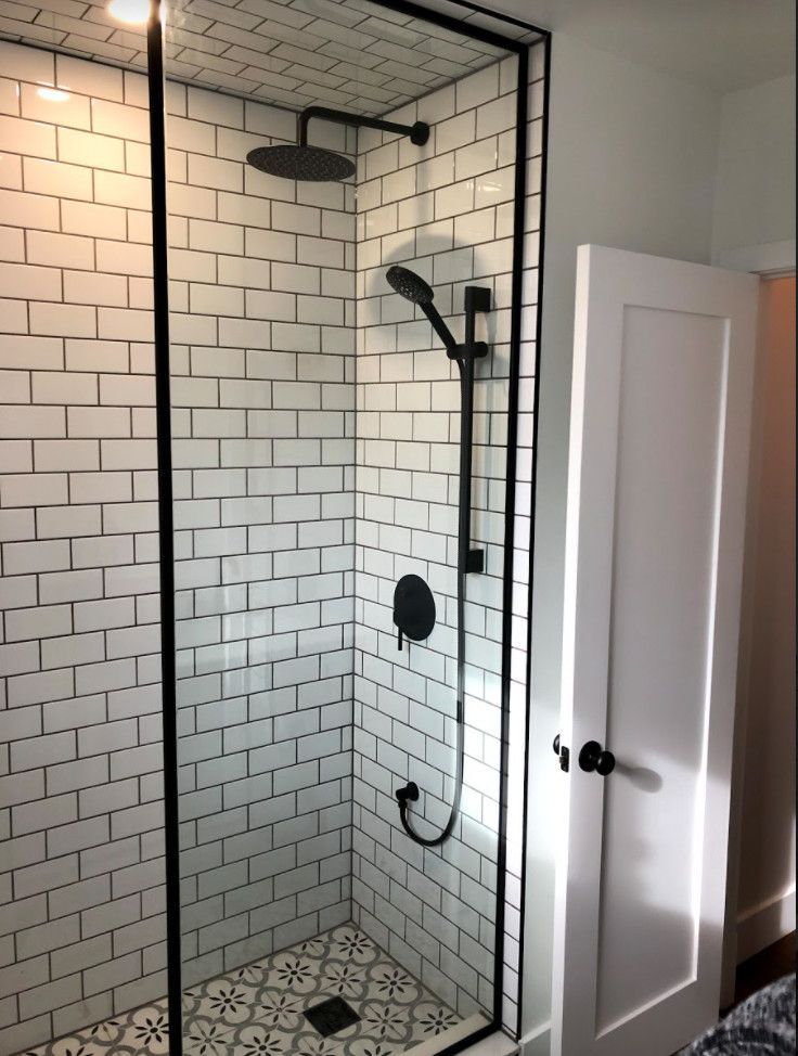 Modern shower with white subway tiles, black fixtures, and patterned floor.