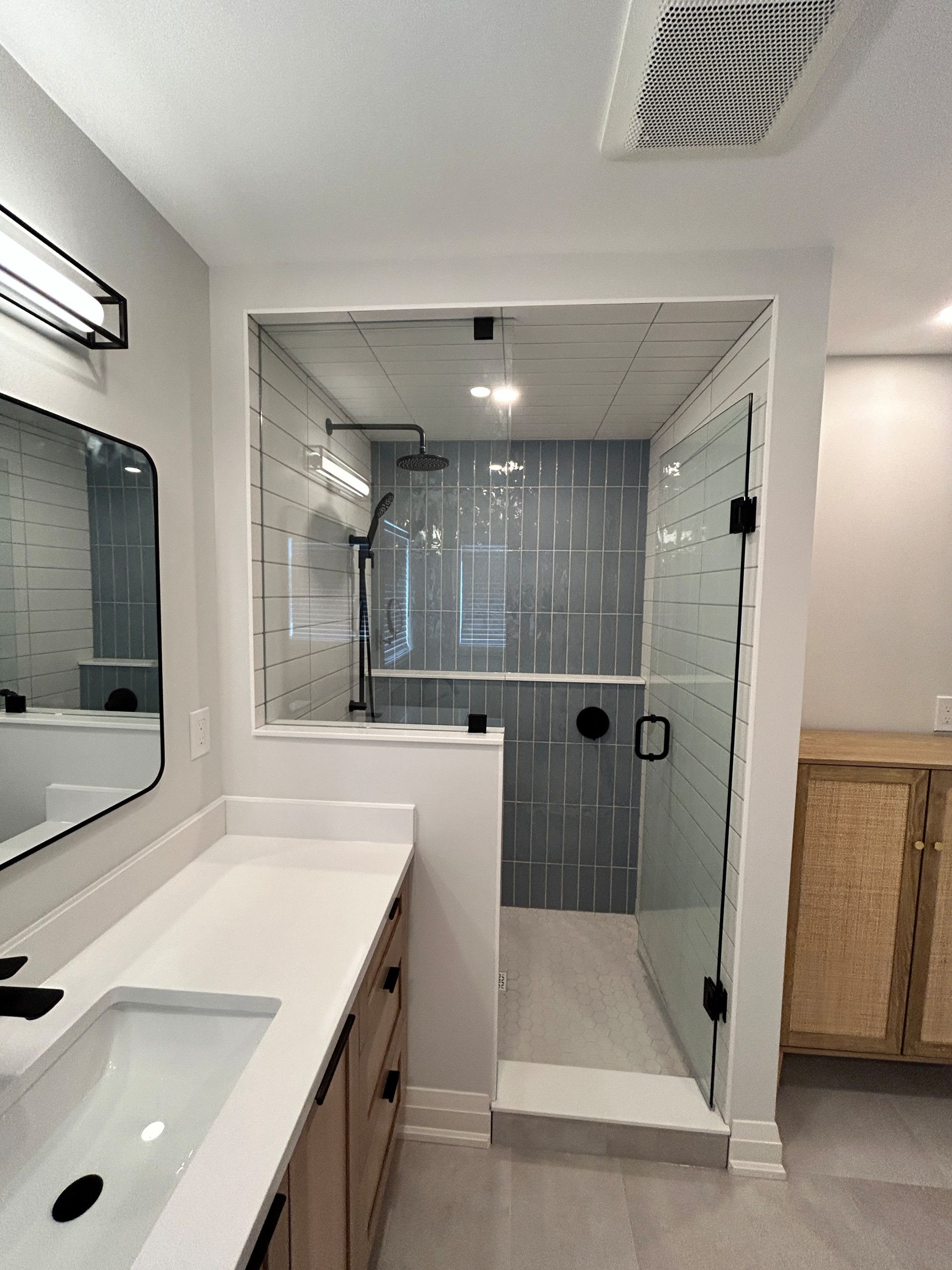Modern bathroom with a glass shower, light gray walls, and a light wood vanity.
