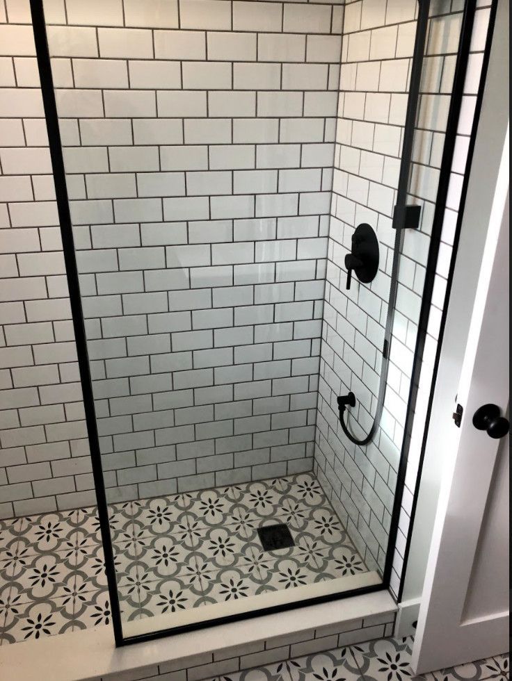 Shower with white subway tile walls, patterned floor tile, and black fixtures.