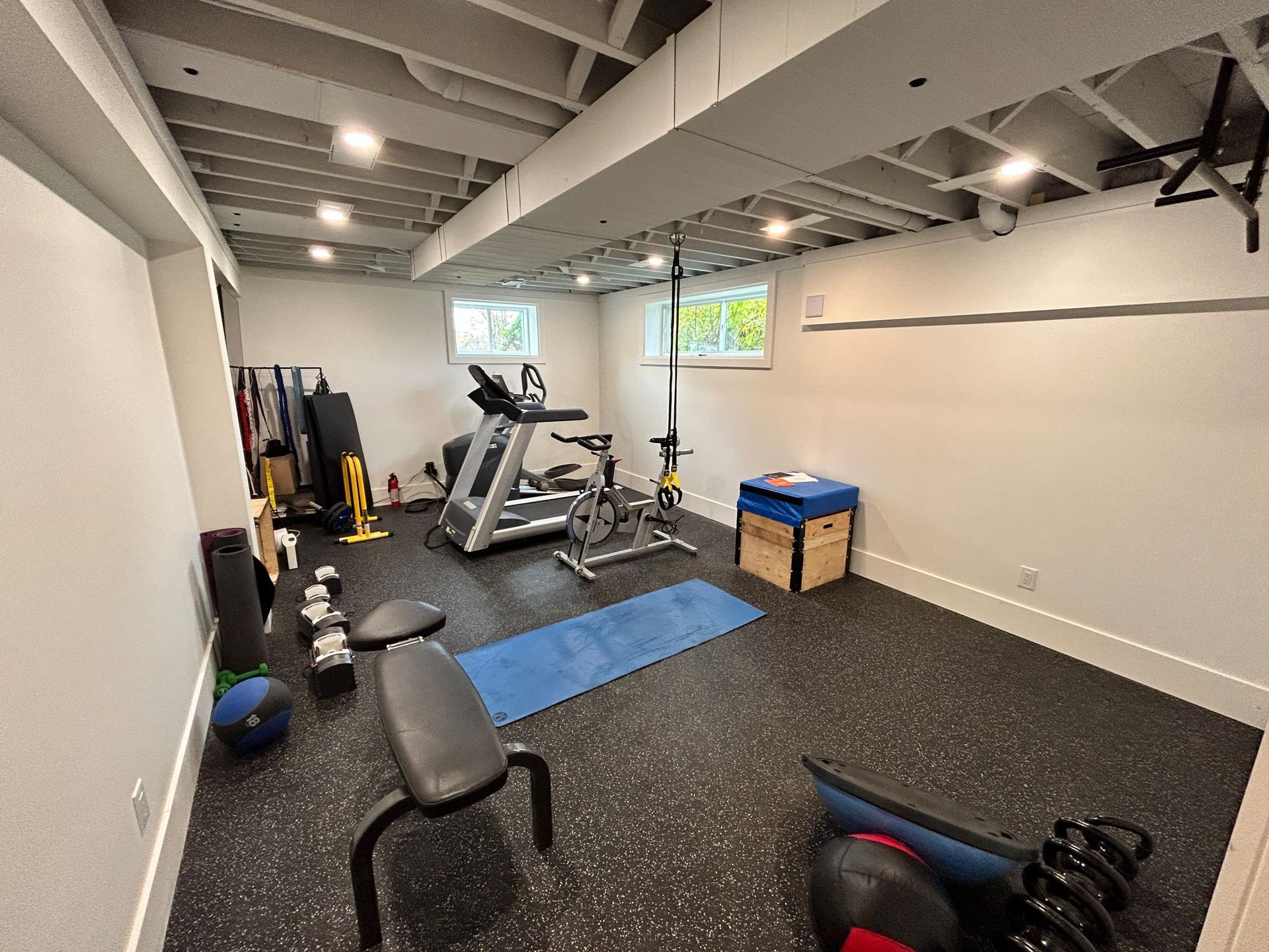 Home gym with weights, treadmill, pull-up bar, and blue exercise mat on rubber flooring.