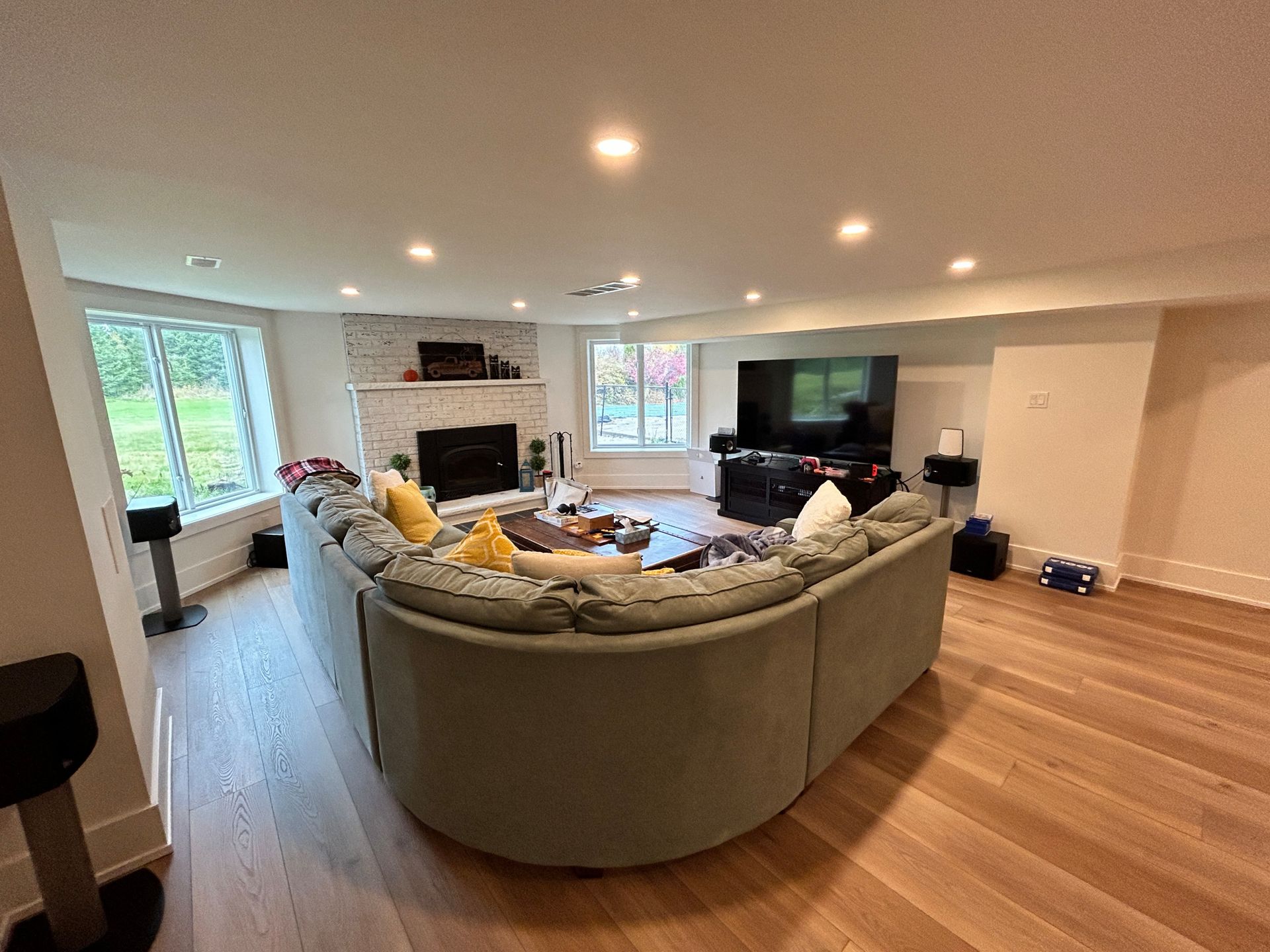 Spacious living room with curved light green sofa, fireplace, large TV, and light wood floors.