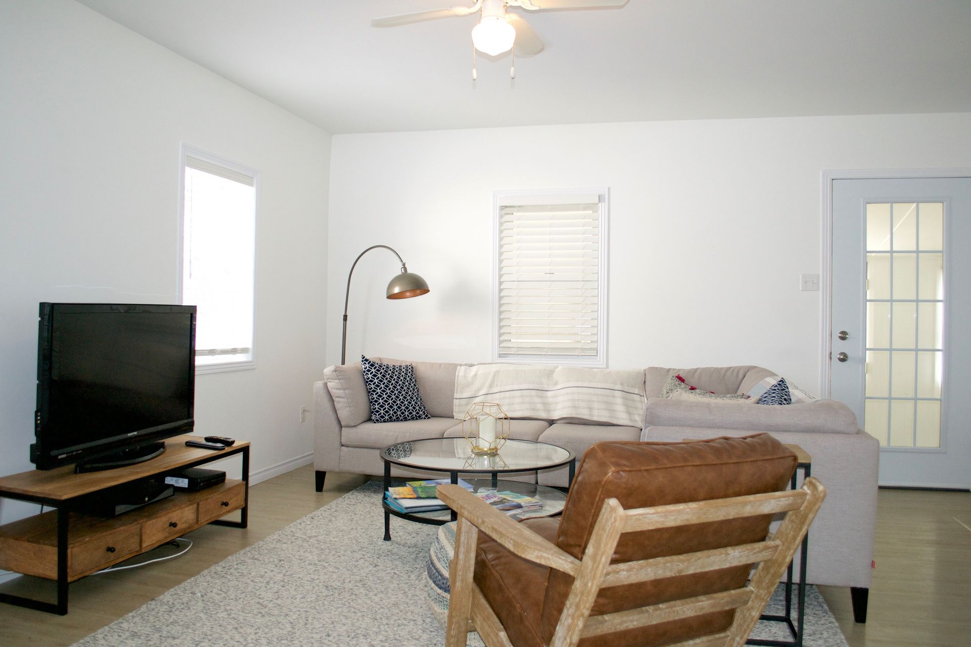 Living room with sectional sofa, armchair, and television; white walls and beige rug.