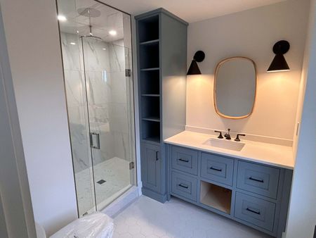 Bathroom with blue vanity, open shelving, a glass shower, and a gold-framed mirror.