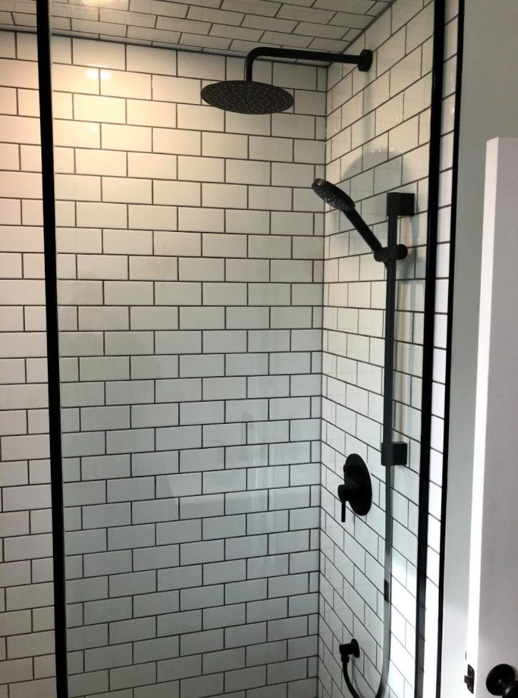 Shower stall with white subway tile, black fixtures, and a glass door.