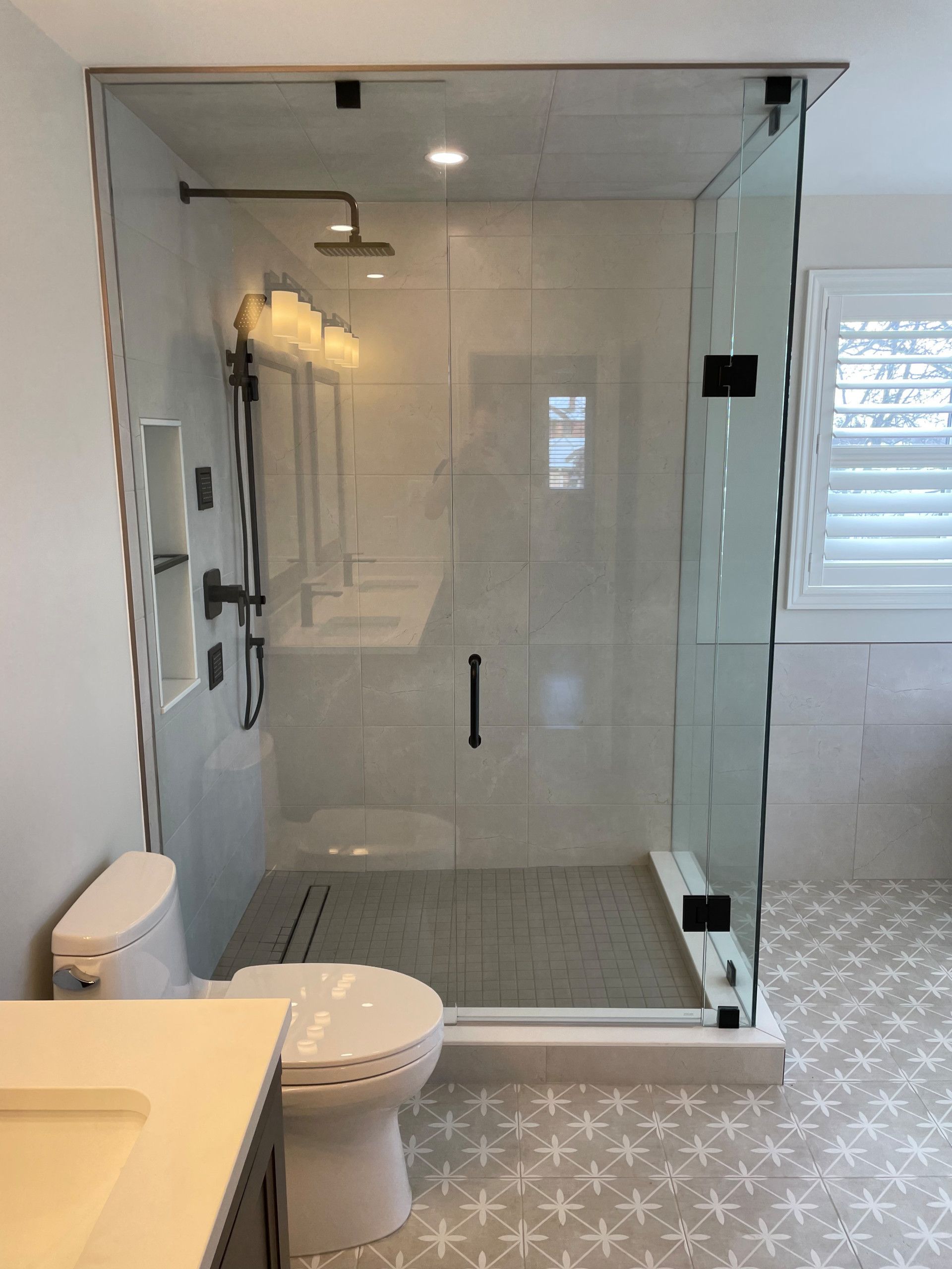 Modern glass shower with black hardware next to a white toilet and a patterned tile floor.