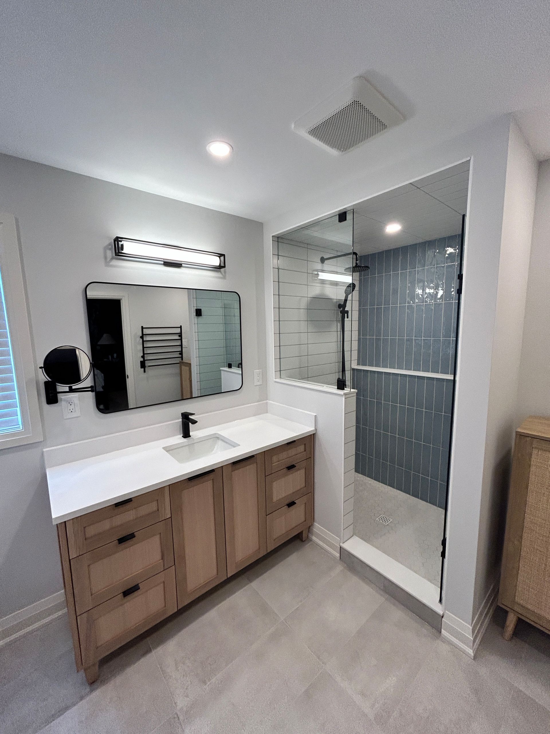 Modern bathroom with wood vanity, glass shower, and light gray walls.