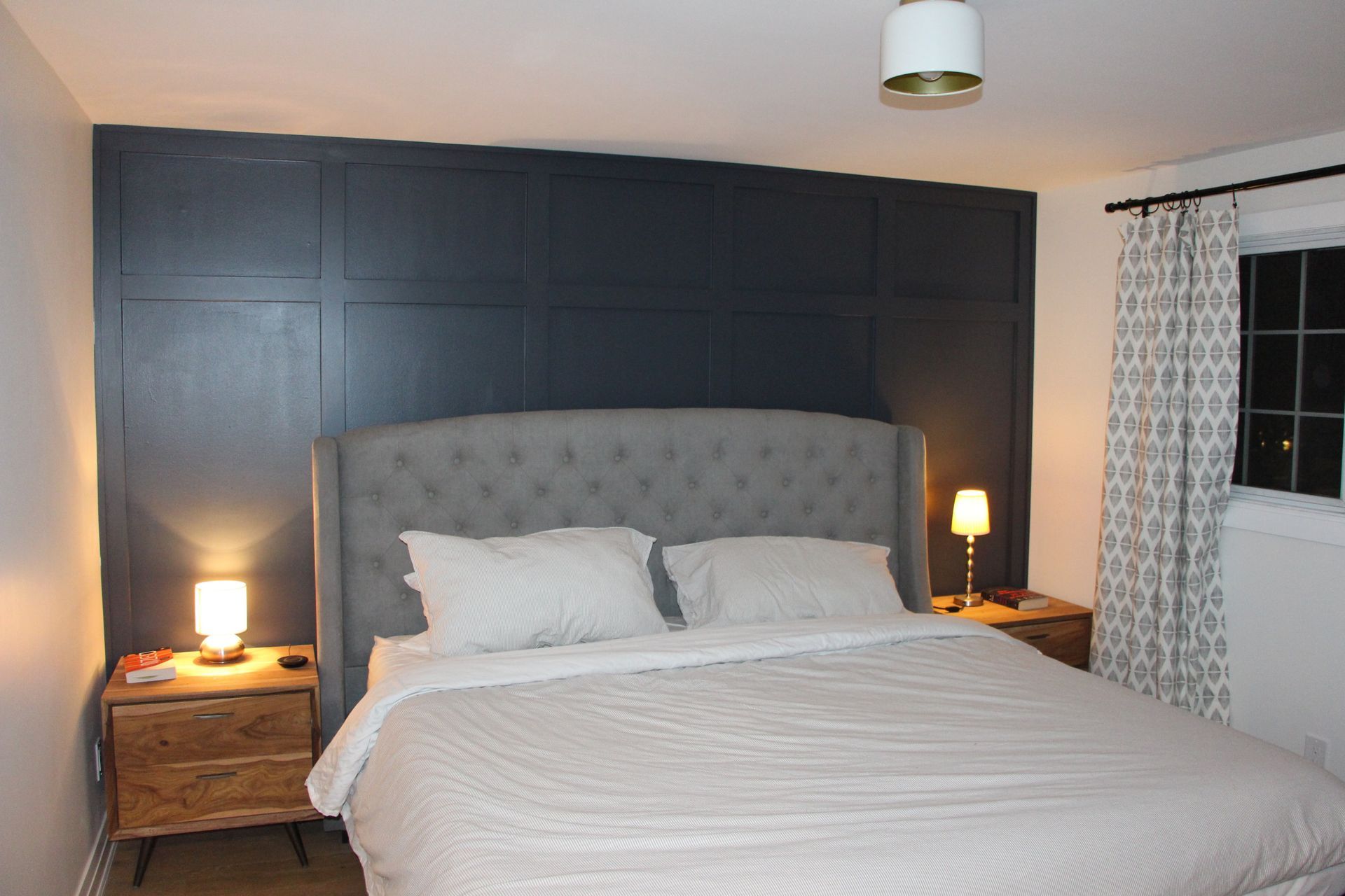 Bedroom with gray tufted headboard, two wooden nightstands, and a dark blue accent wall.
