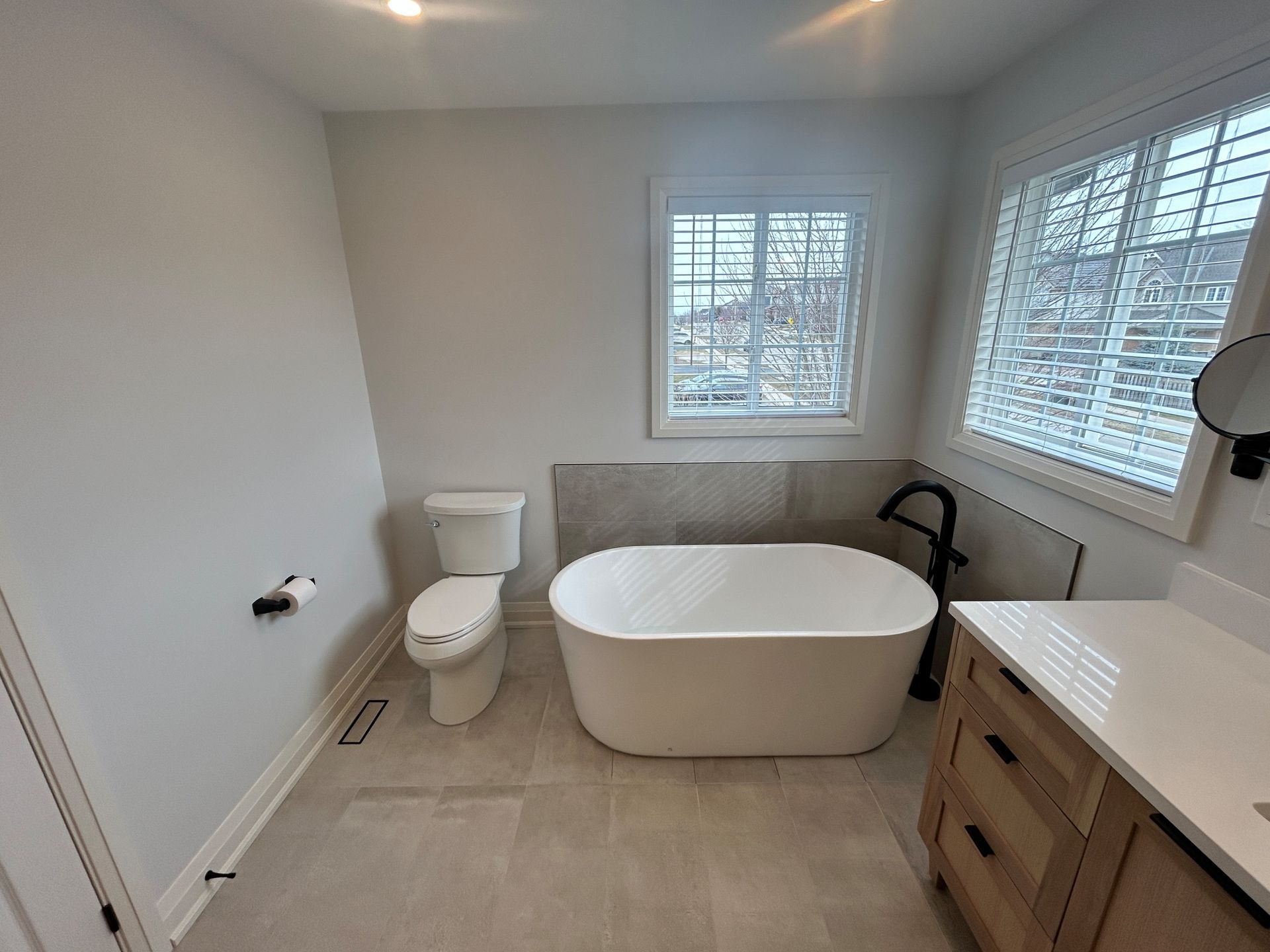 Modern bathroom with a white tub, toilet, and vanity against gray walls and flooring.