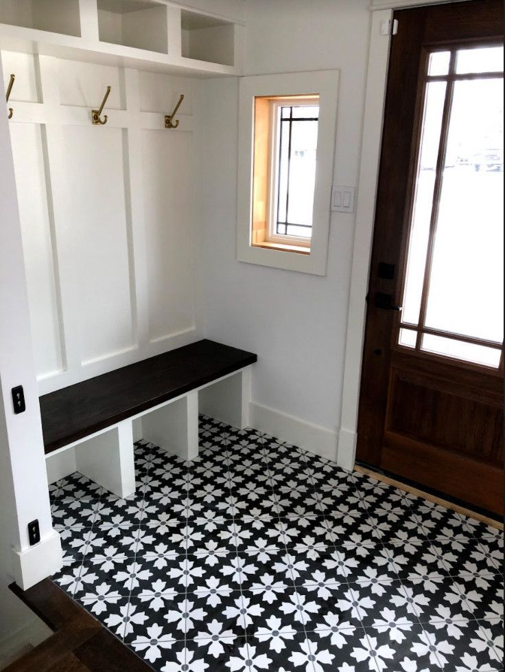 Entryway with black and white patterned floor, white wainscoting, bench, and wooden door.