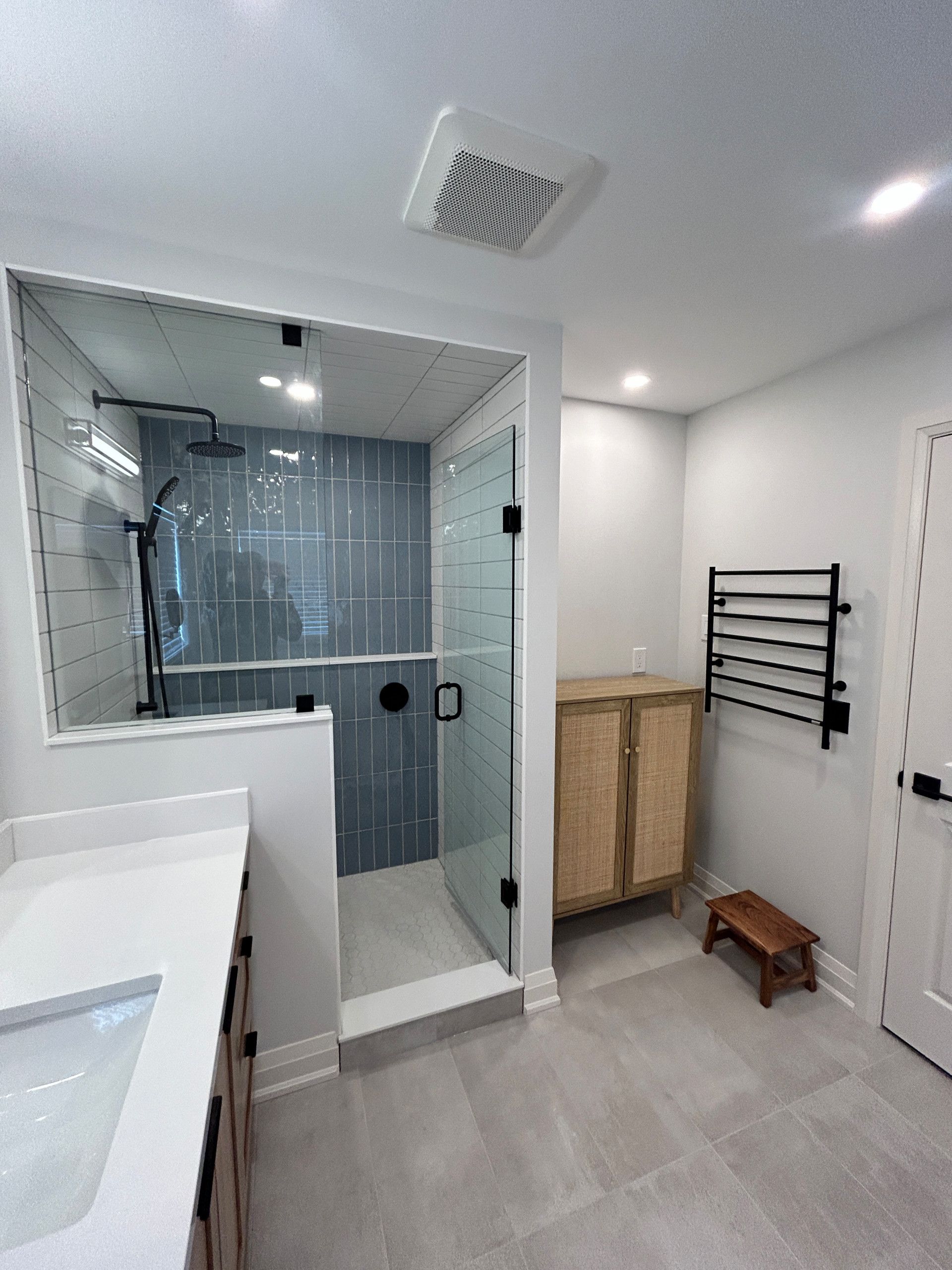 Modern bathroom with a glass shower, gray tiles, and a wood cabinet.