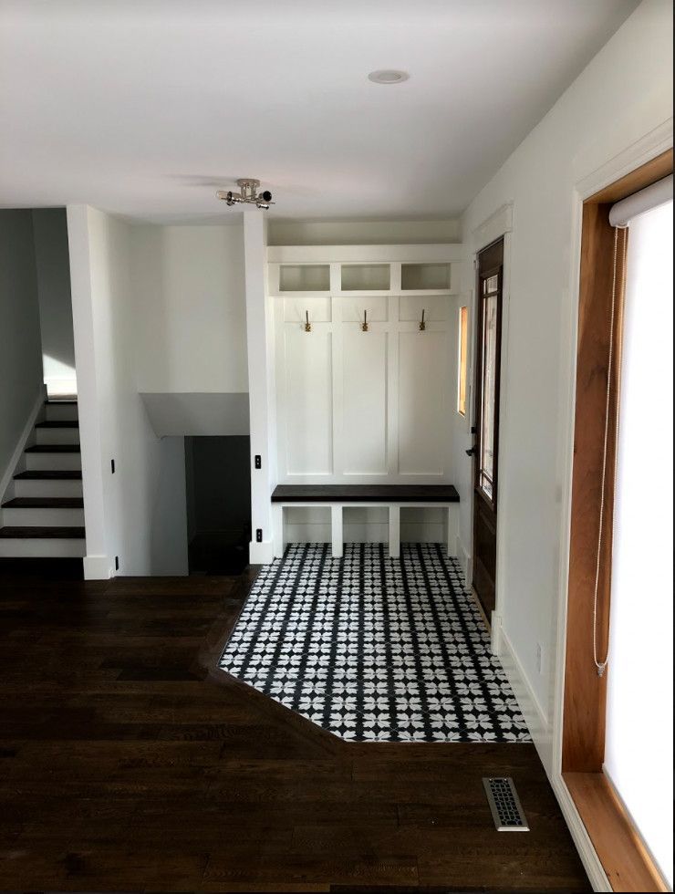 Hallway with white built-in coat rack and bench on patterned tile, dark wood flooring, stairs to the left.