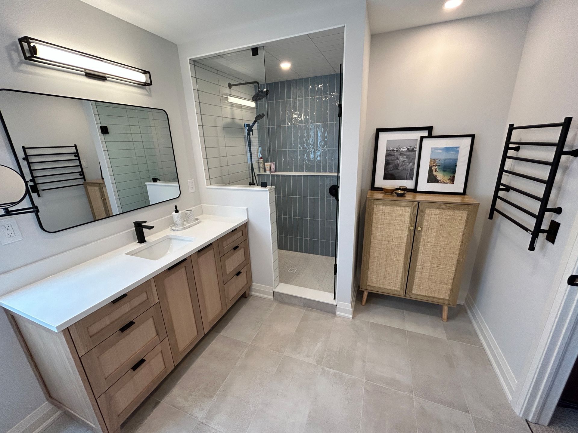 Modern bathroom with light wood vanity, glass shower, and gray tiled floor.