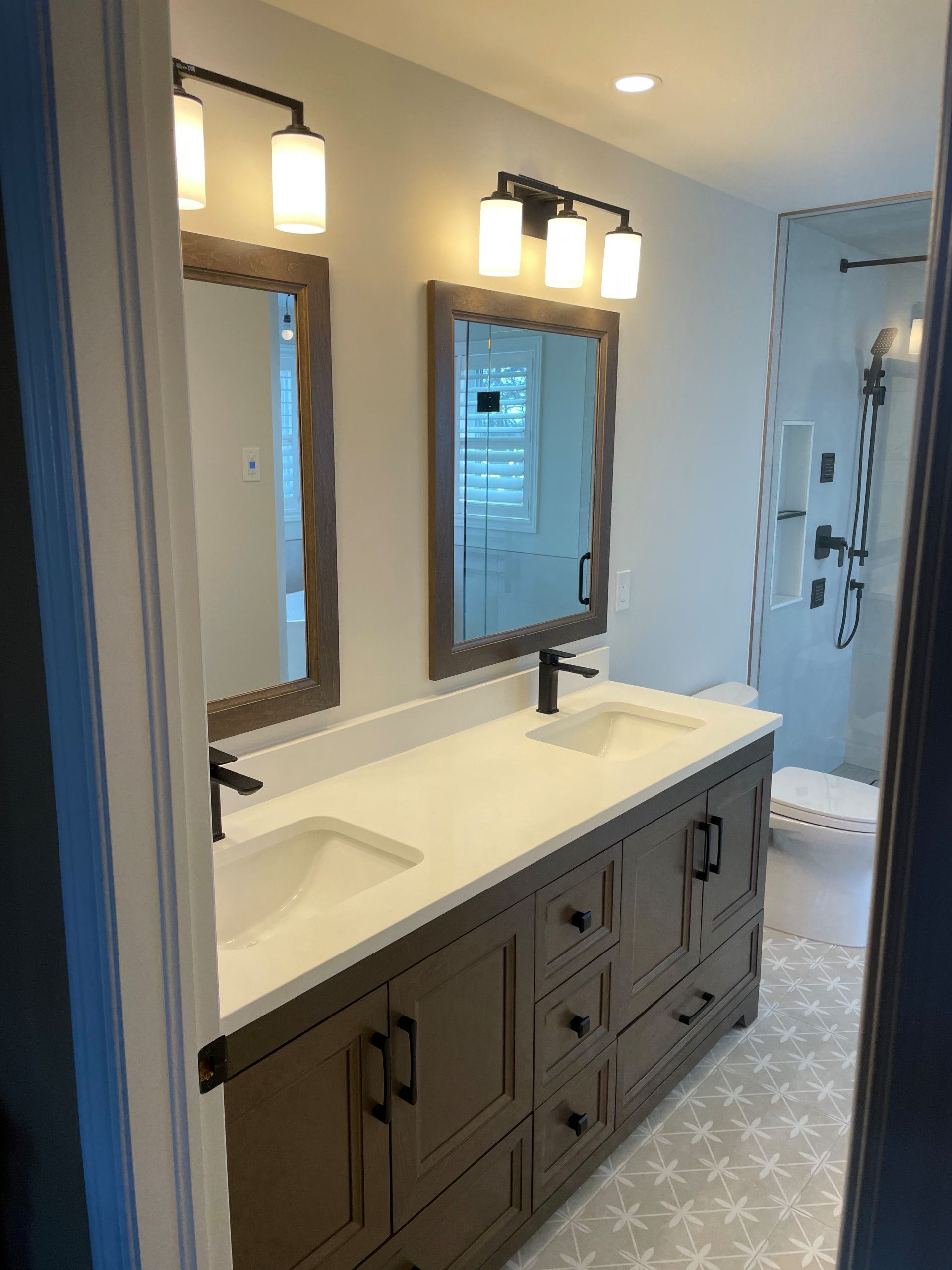 Bathroom with a double vanity, two mirrors with lights, and a walk-in shower.