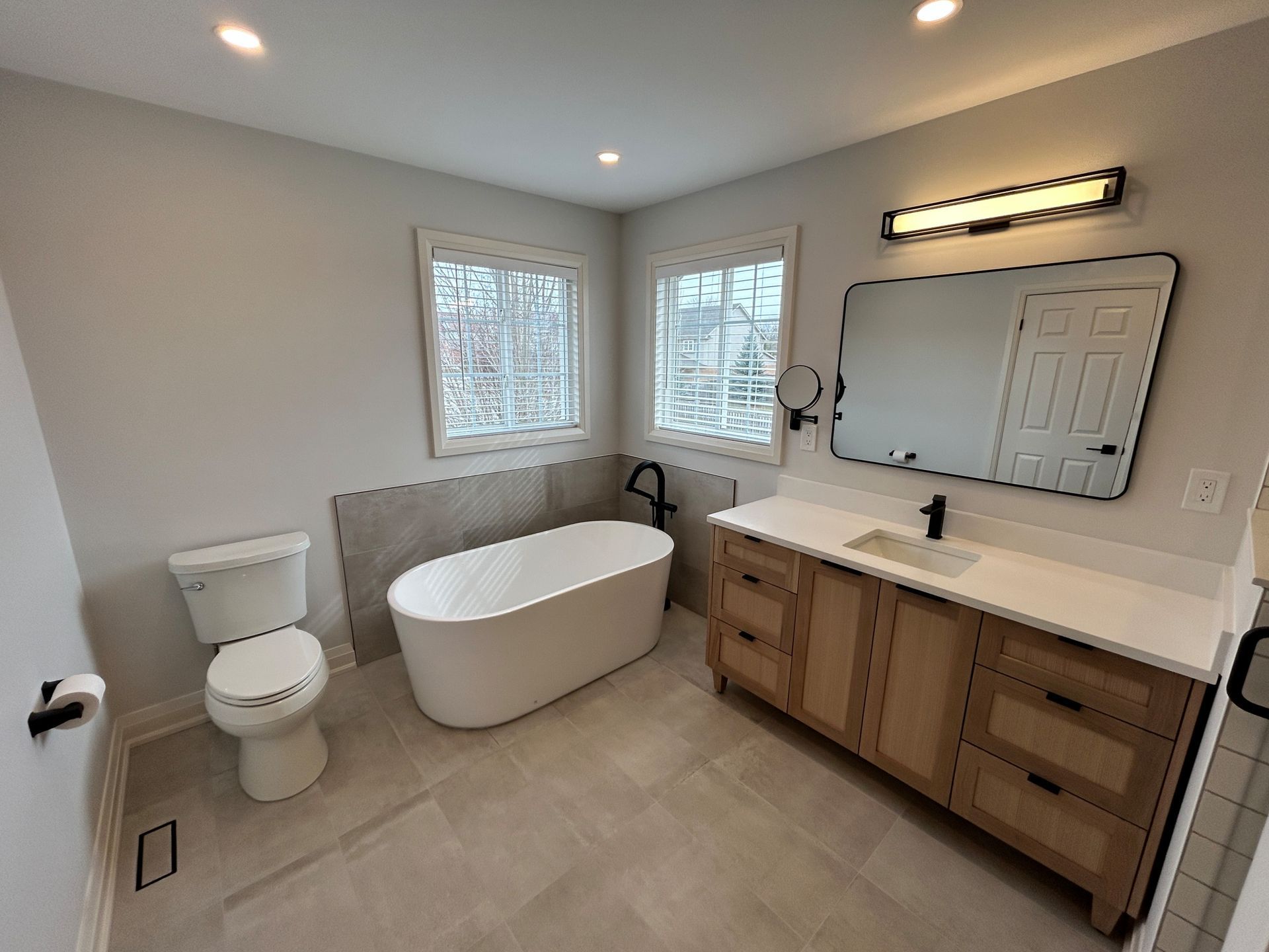 Modern bathroom with a white tub, wooden vanity, and gray tile flooring.