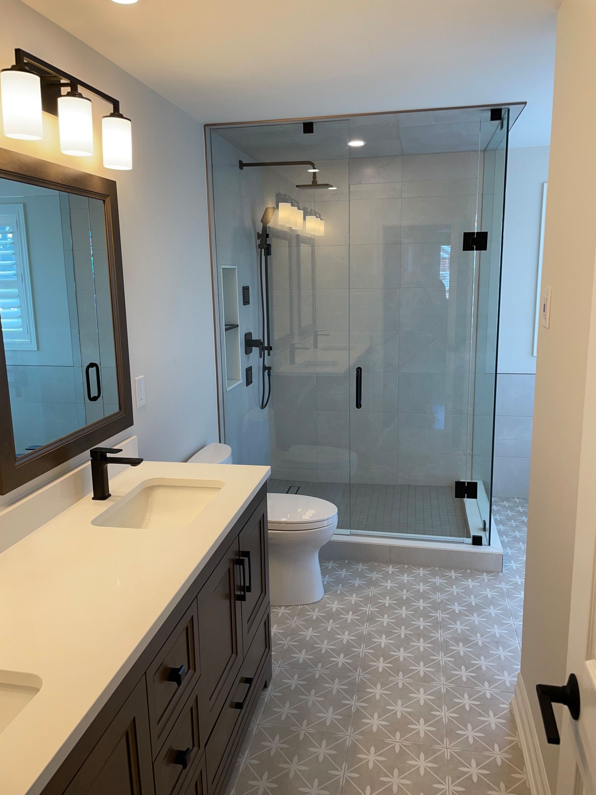 Modern bathroom with gray vanity, glass shower, and patterned floor.