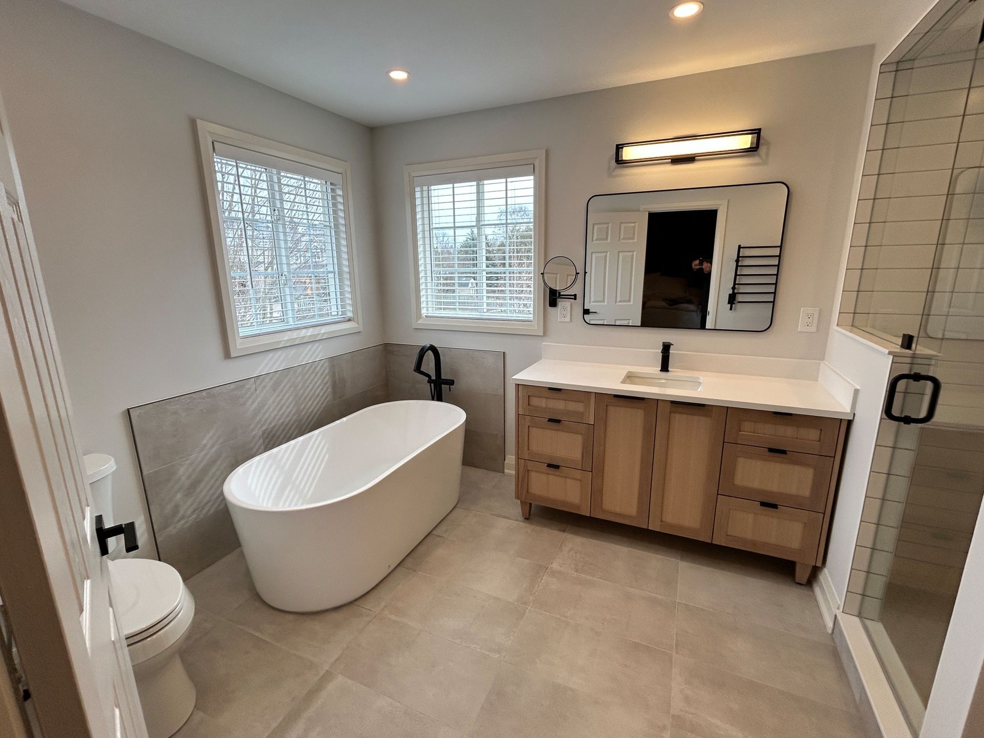 Modern bathroom with a freestanding tub, wood vanity, and large mirror.