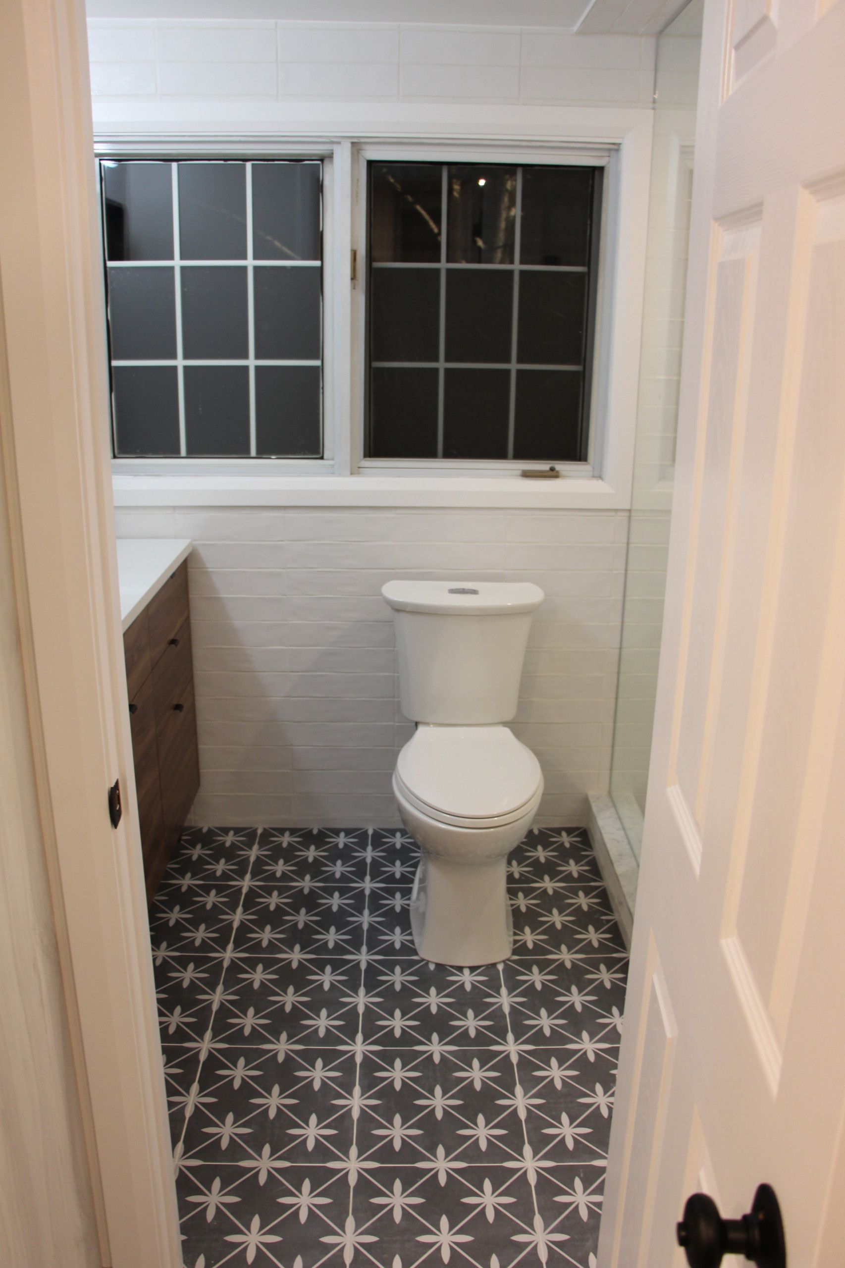 Bathroom with white toilet, patterned floor, window, and partially visible vanity.