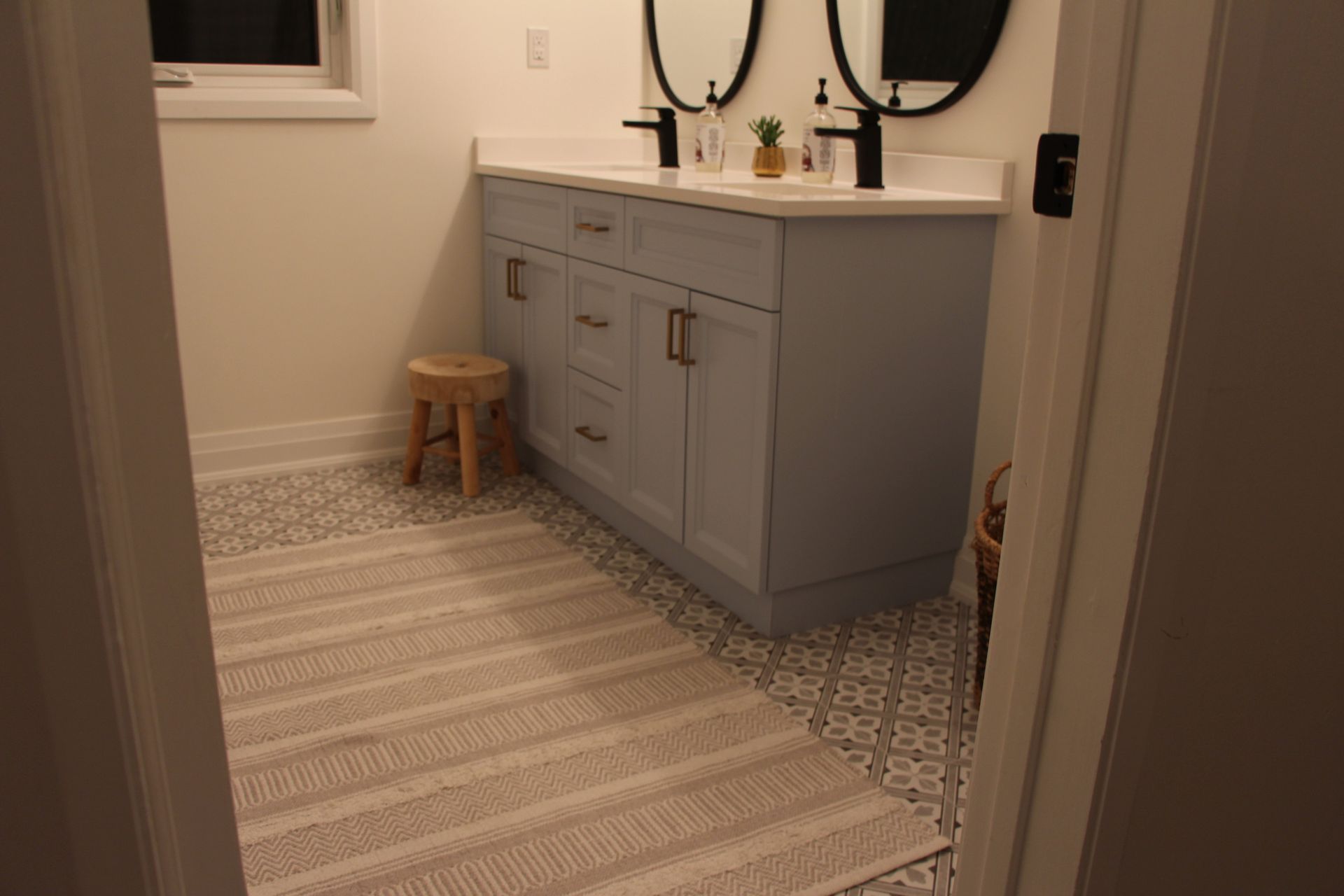 Bathroom with light blue vanity, patterned floor, and cream rug.