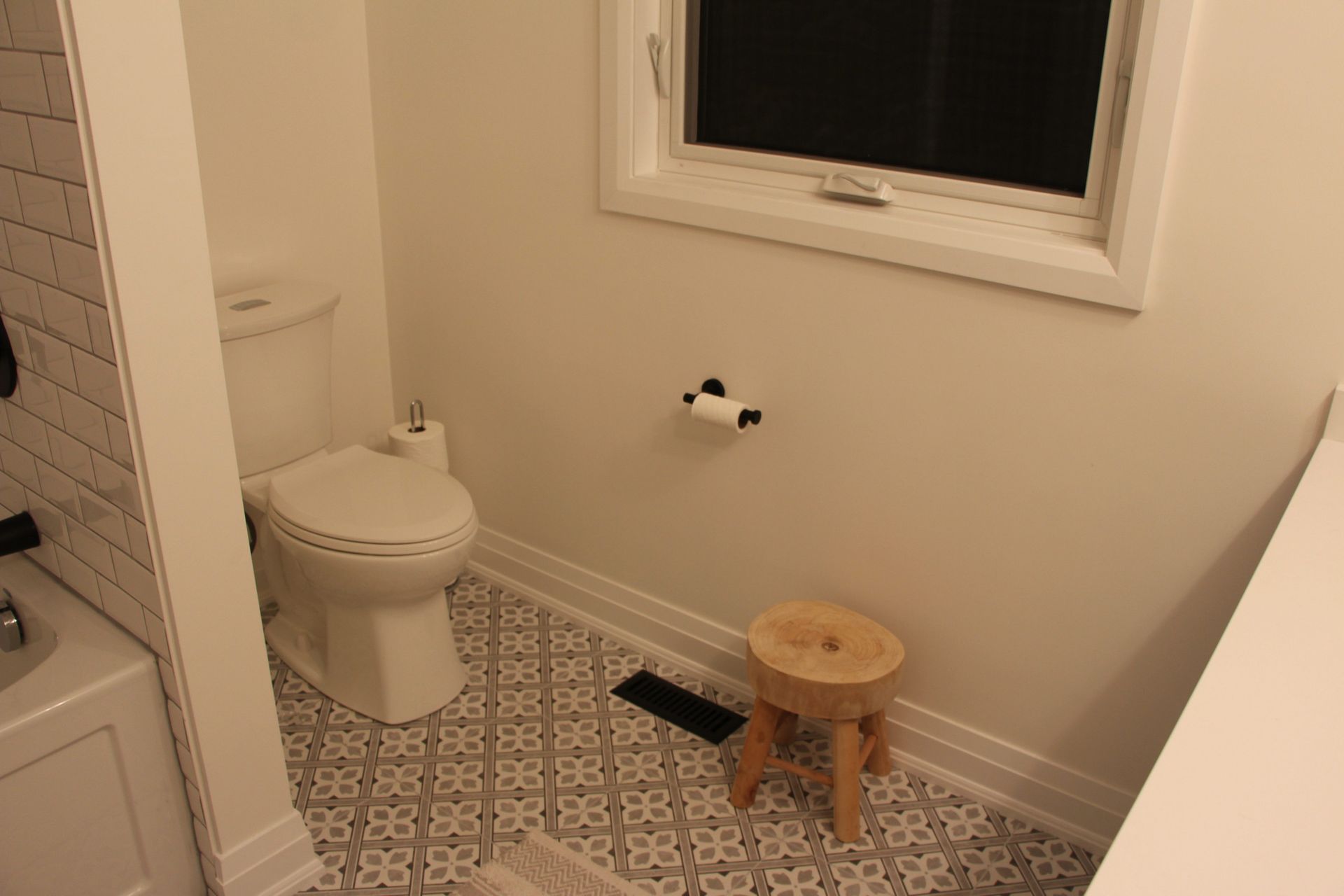 Small bathroom with patterned tile floor, toilet, stool, and window.