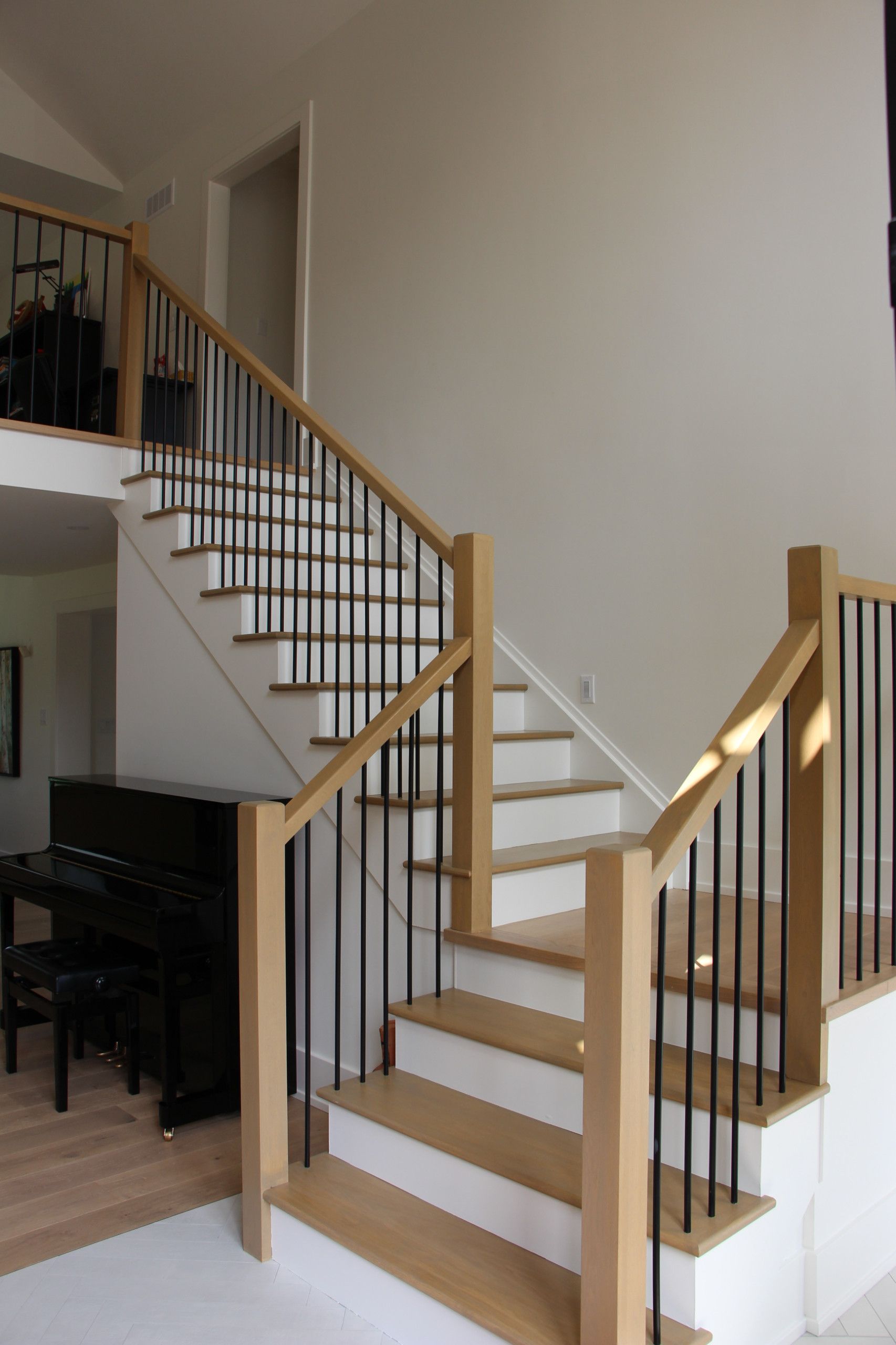 Staircase with wood and black metal railing. A grand piano sits near the stairs in a light-filled home.