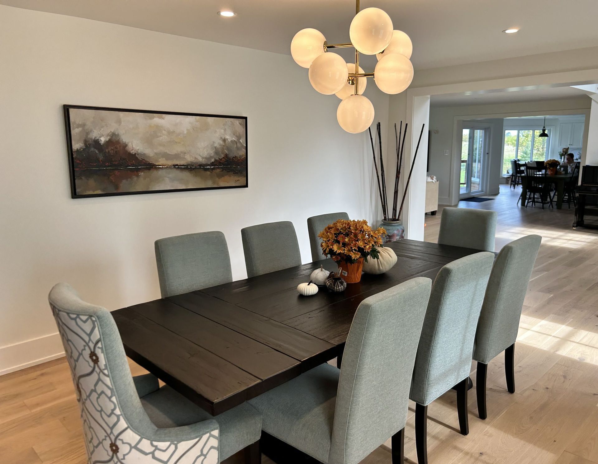 Dining room with a dark table, eight blue chairs, art, and a globe chandelier.