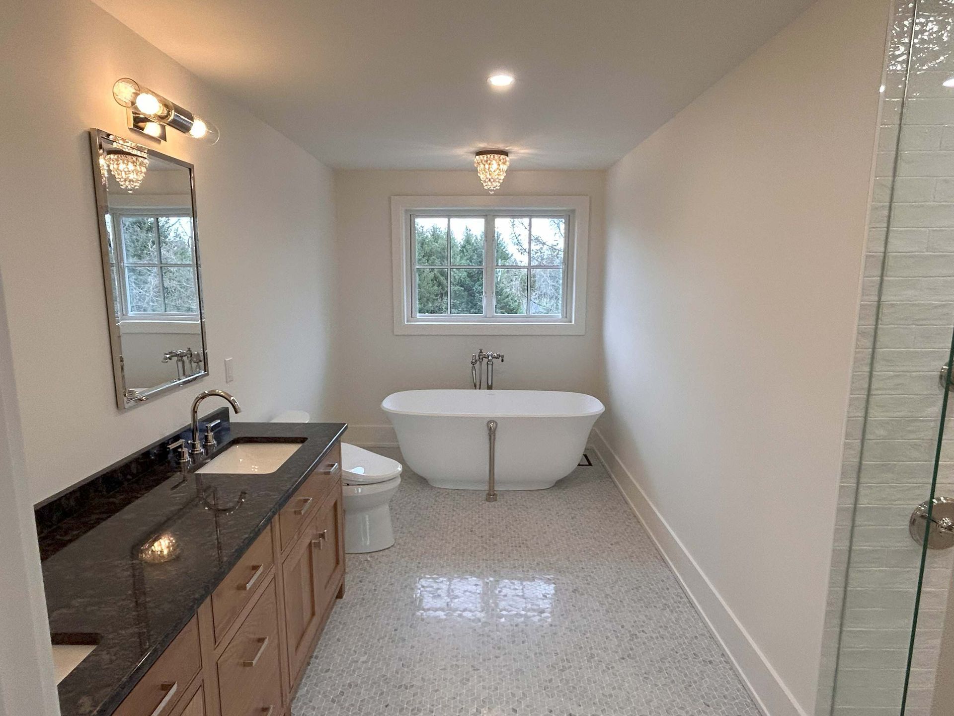 Bathroom with a white tub, vanity, toilet, and speckled floor. Window above the tub.
