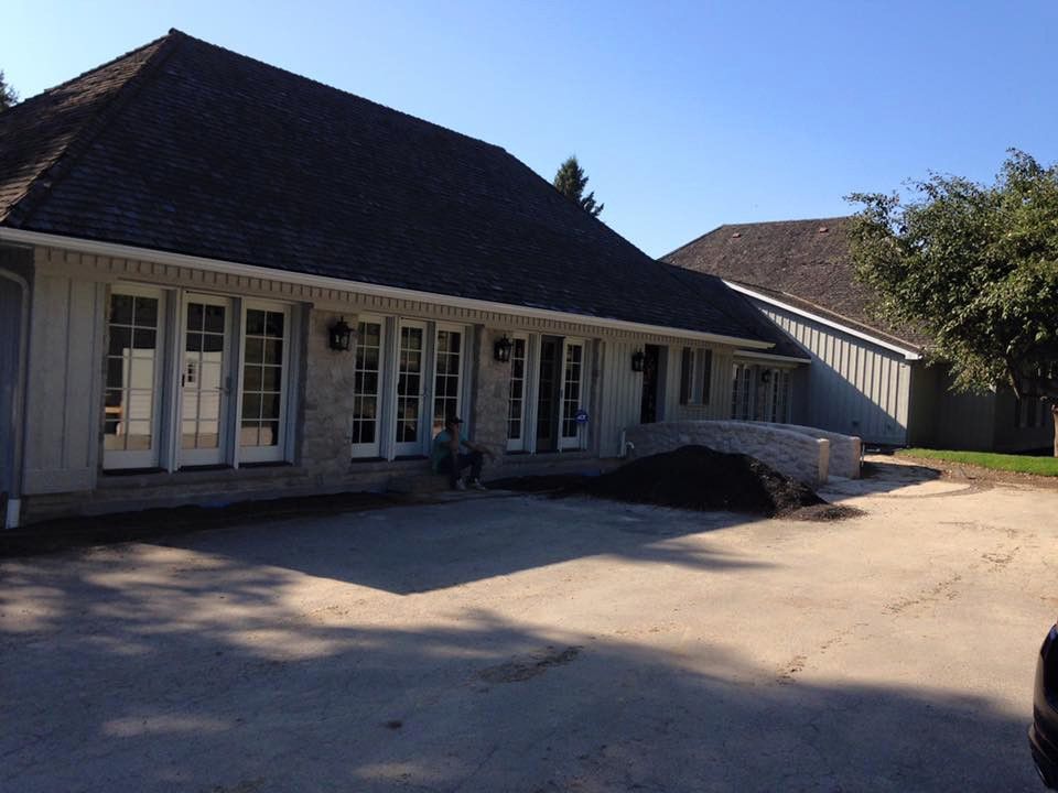 A low, light-colored building with many windows. A person sits on the steps, and a dark roof is overhead.