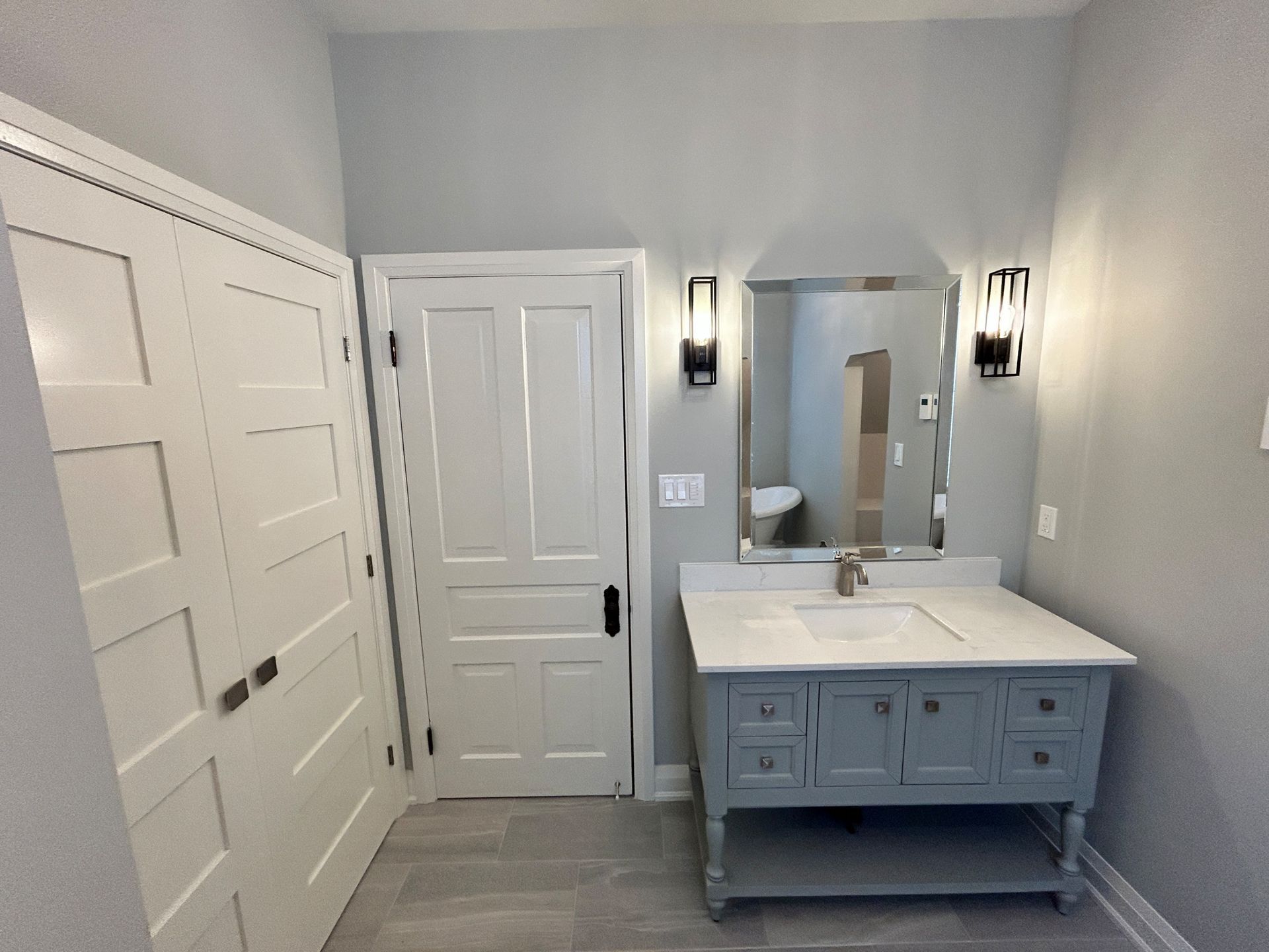 Bathroom with gray walls, white trim, blue vanity, mirror, and closet.