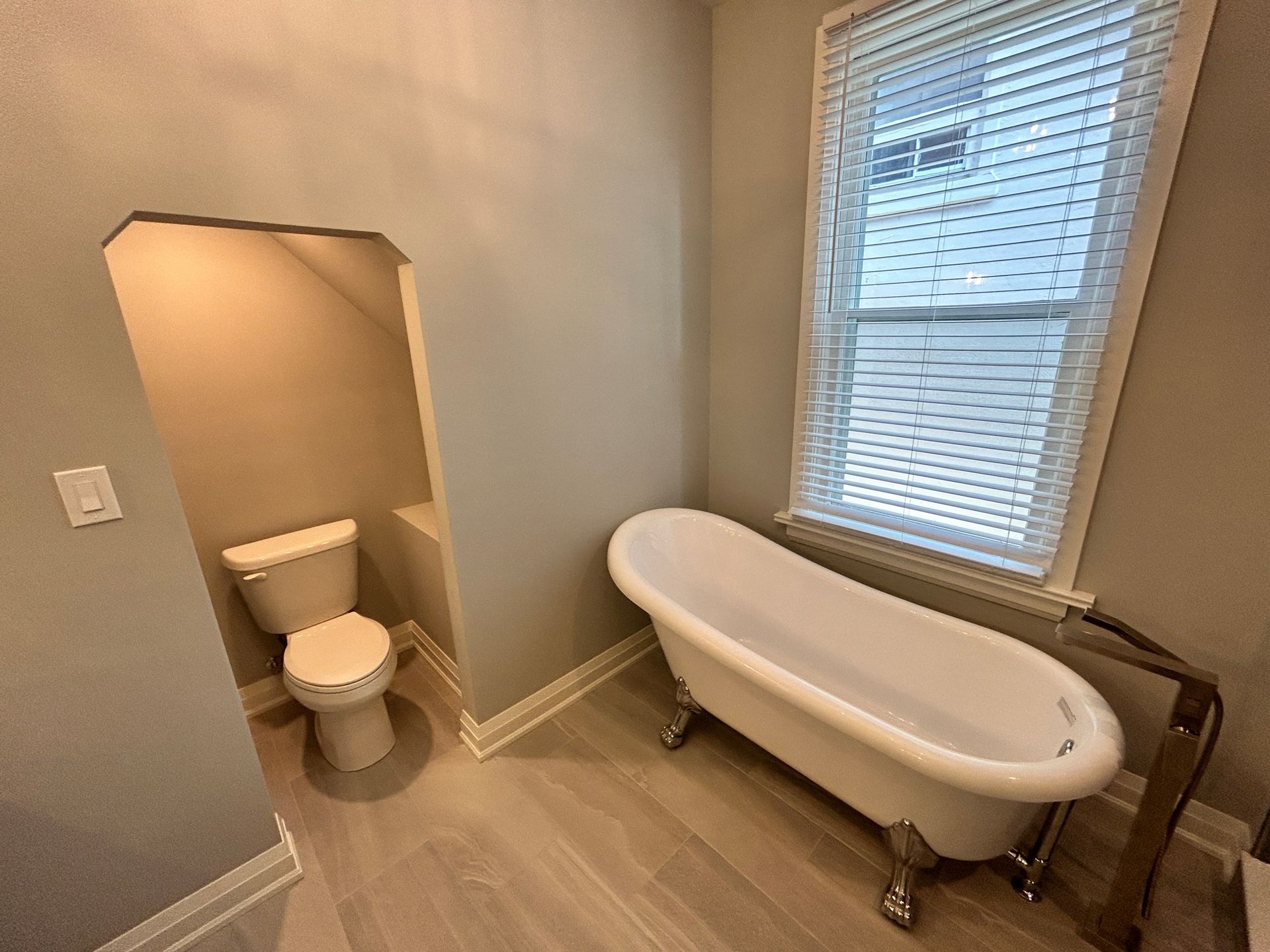 Bathroom with a vintage clawfoot tub, toilet in a nook, and a window with blinds.
