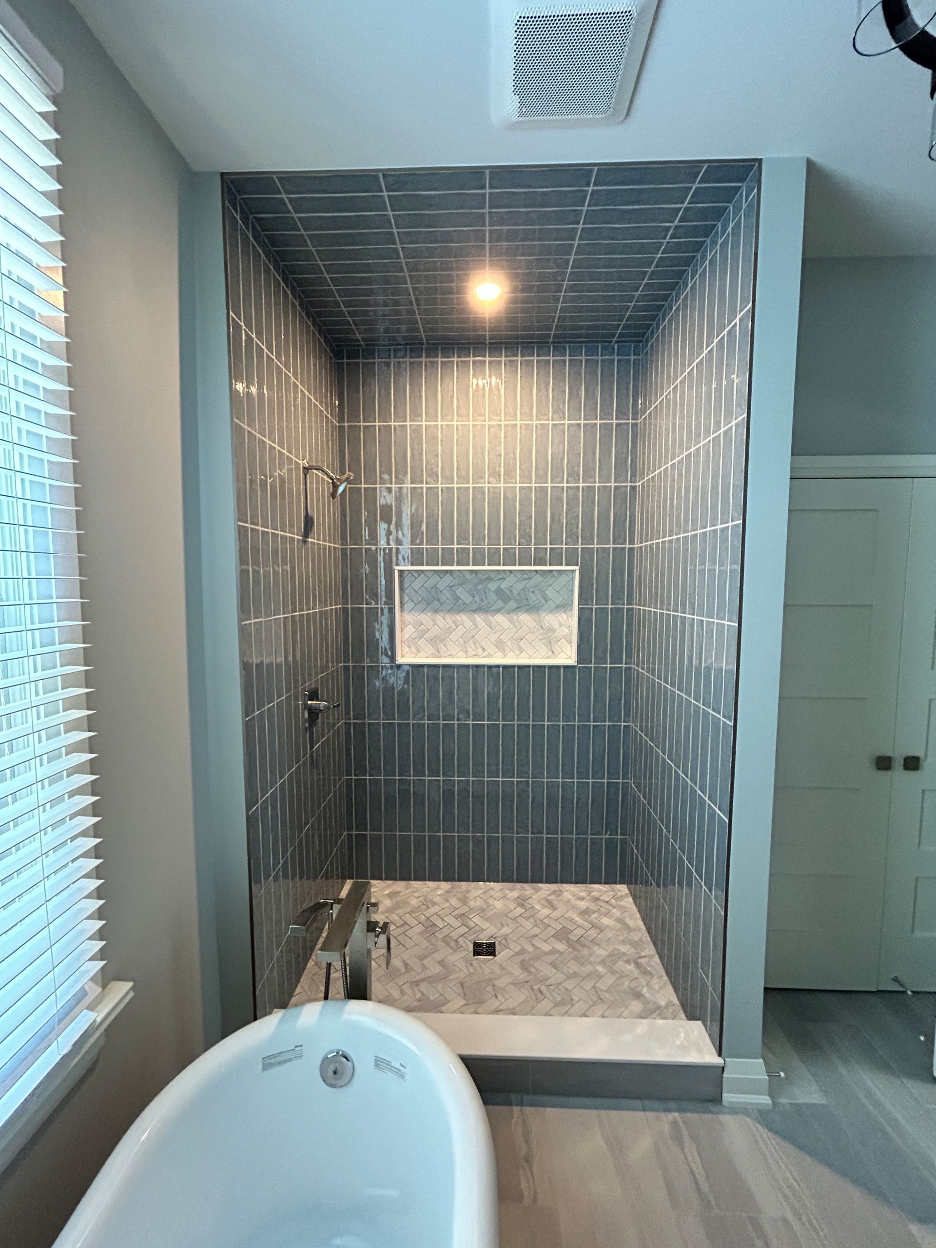 Bathroom shower with gray tile and ceiling, bathtub in foreground, and a window.