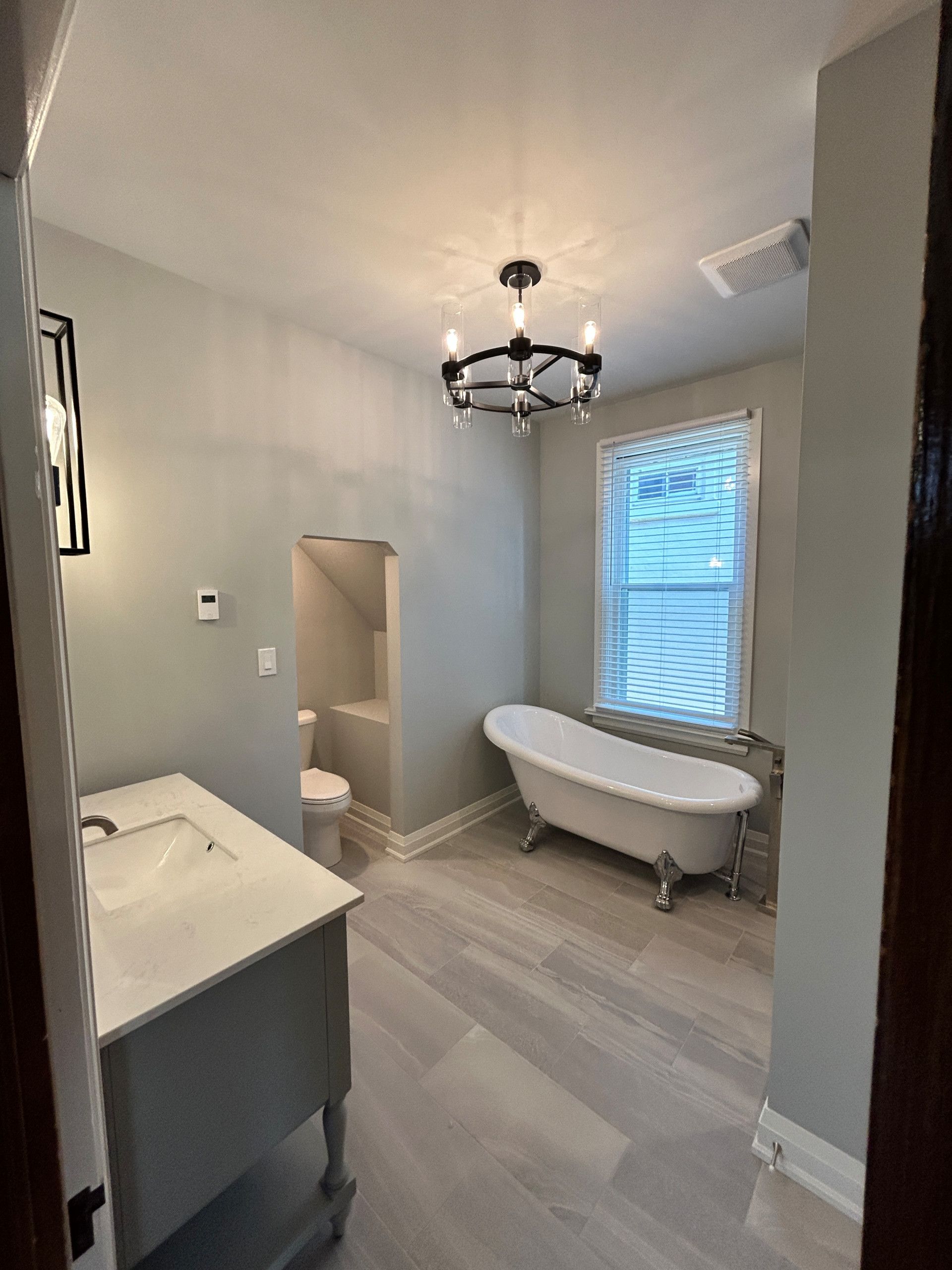 Bathroom with freestanding tub, vanity, and chandelier; light gray walls and floor.