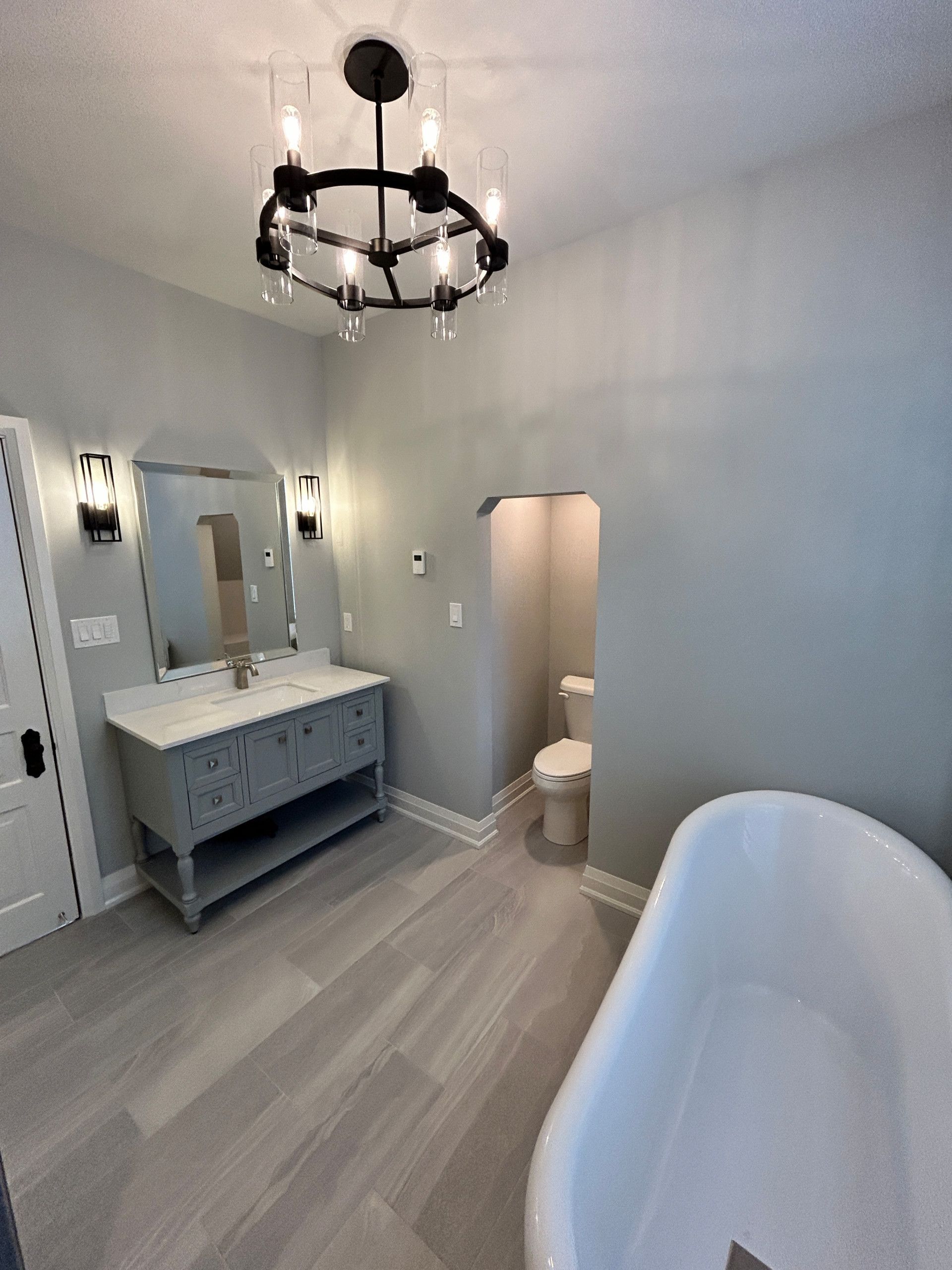 Bathroom with a gray vanity, white bathtub, and a black chandelier.