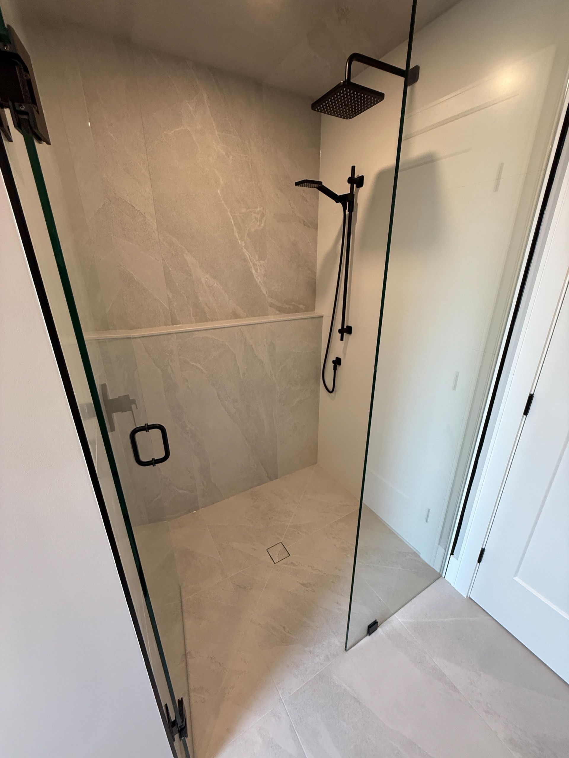 Modern shower with a glass door, black fixtures, and gray tile walls and floor.