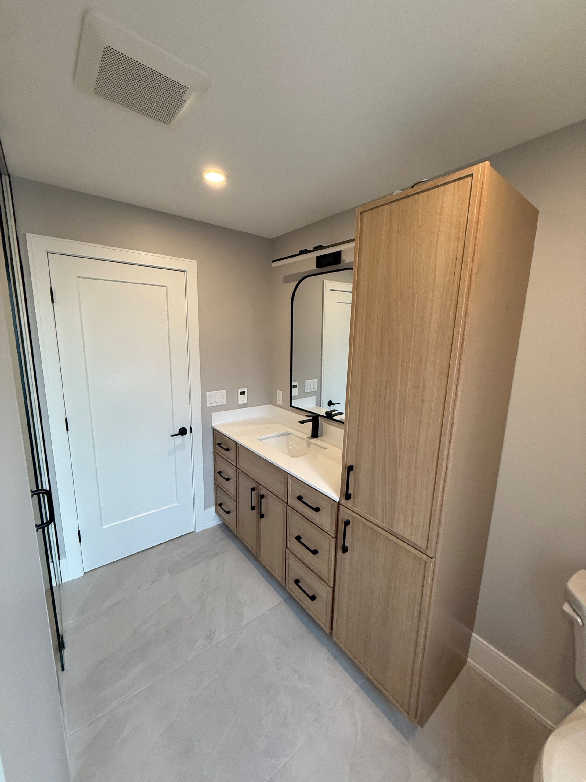 Bathroom with light wood cabinetry, a white vanity, and a black-framed mirror.