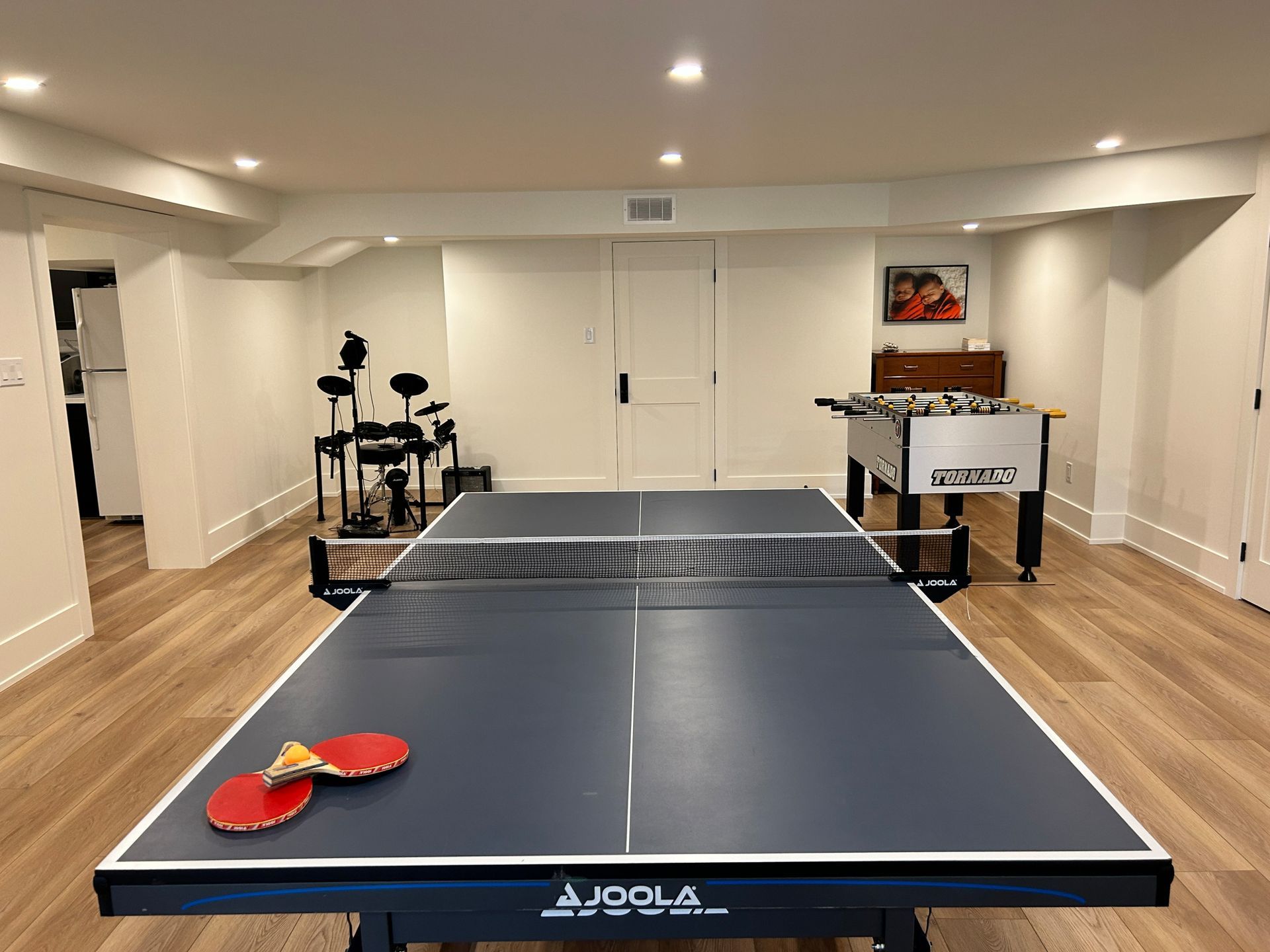 Table tennis table in a finished basement with drum set and foosball table.