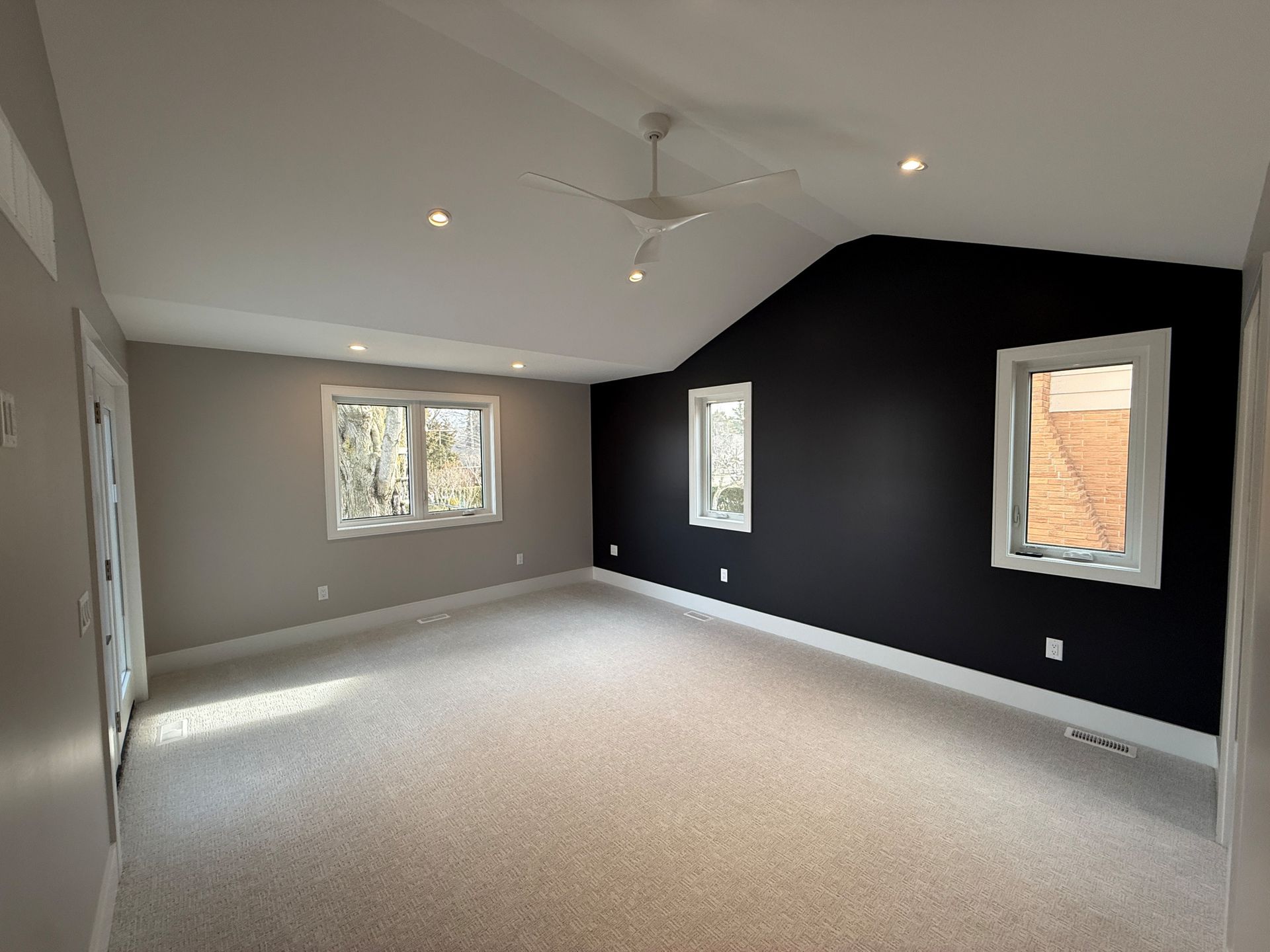 Spacious, newly renovated bedroom with gray walls, a black accent wall, white trim, windows, and beige carpet.